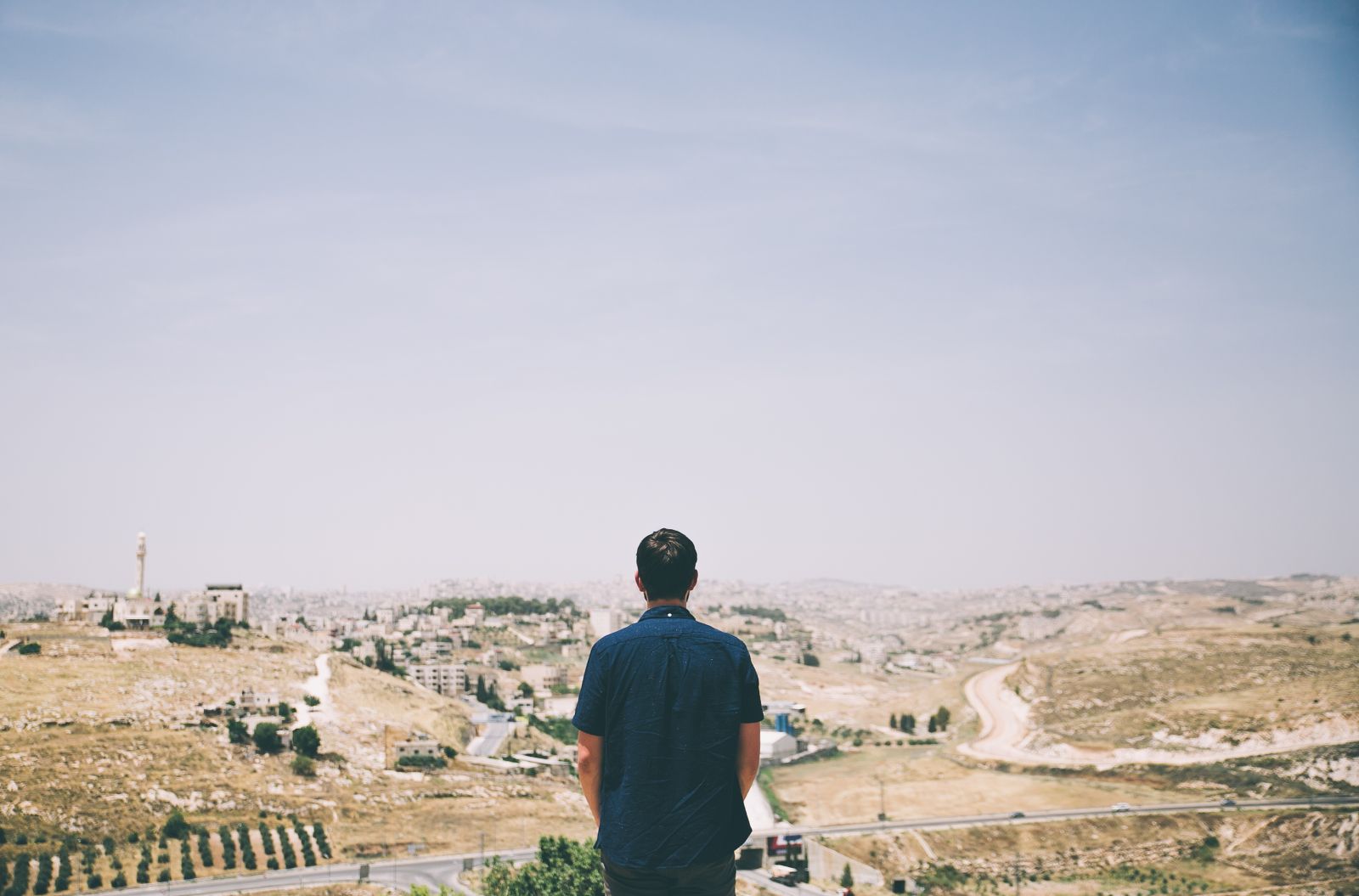 Everything You Need to Know About NUA Films A man standing with his back to the camera looking out on a diverse landscape of hills and fields and buildings.