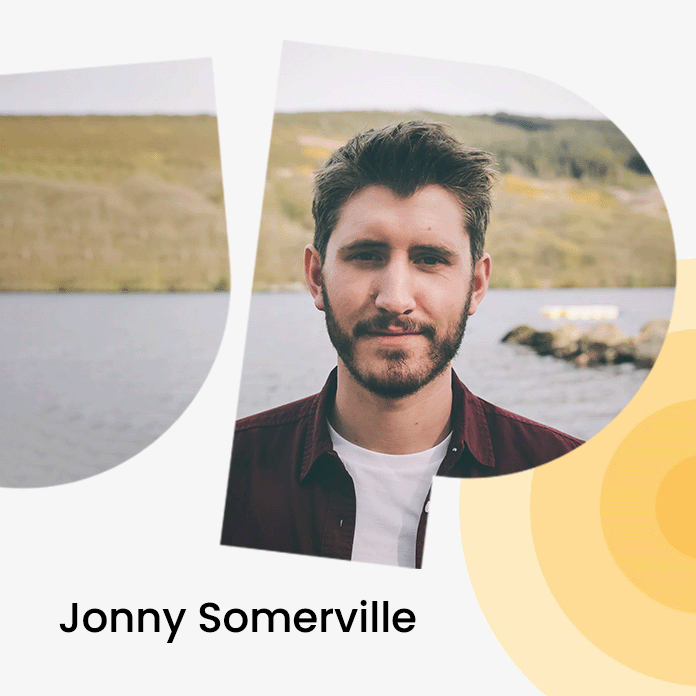 A man with short hair and a beard stands by a lake, with hills in the background. Text reads "Jonny Somerville."