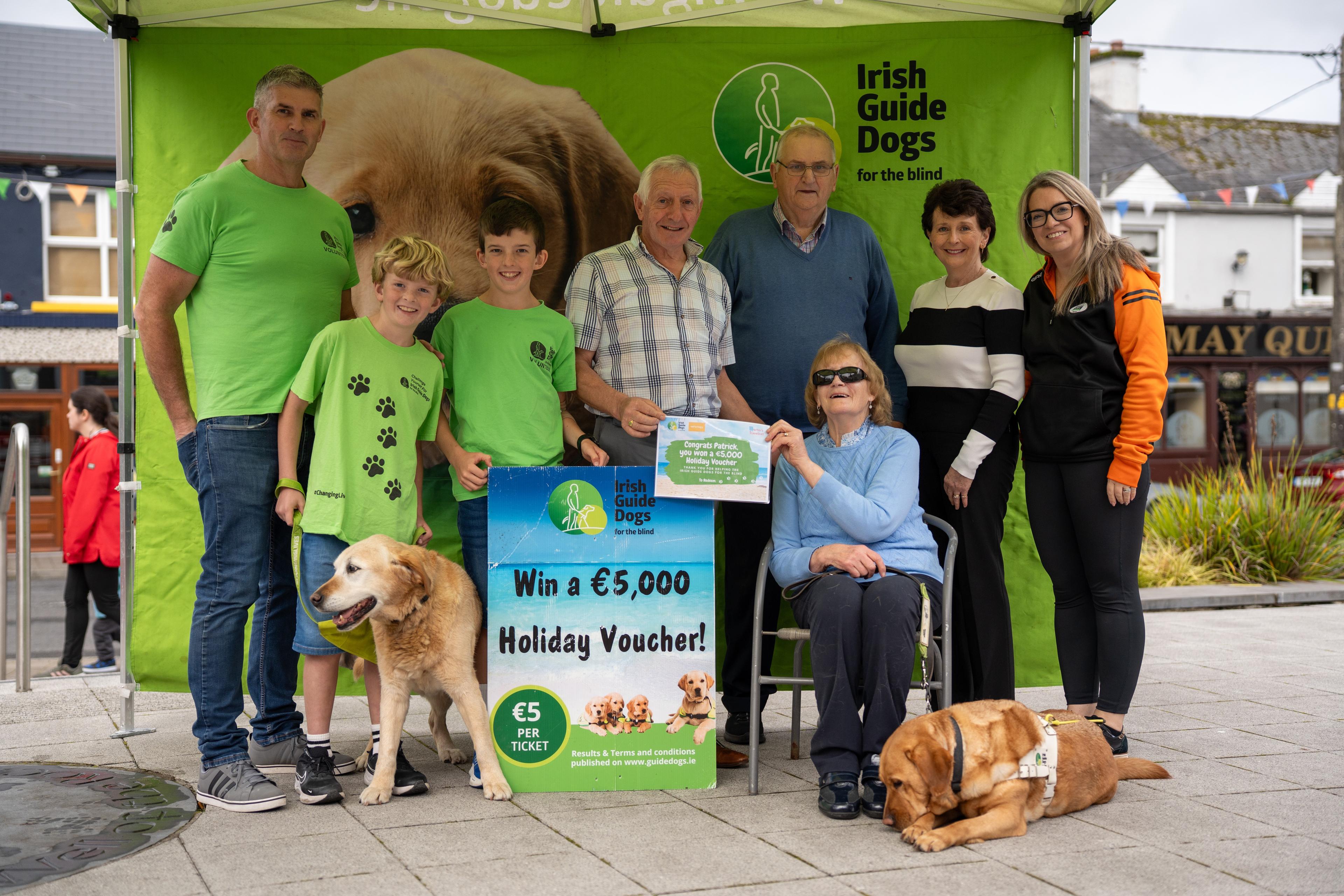 Monica is pictured presenting a €5,000 holiday voucher to the winner of our raffle, Patrick Coleman. Also in photo are (l-r) Ray Wims, Sam Wims with Guide Dog Guinness, Zac Wims, Patrick, Monica with Piper, Nathy Wims, Collette Coleman and Louise Kilbane (chairperson of Tubbercurry Old Fair Day Committee). Photo by Barry Clavin.