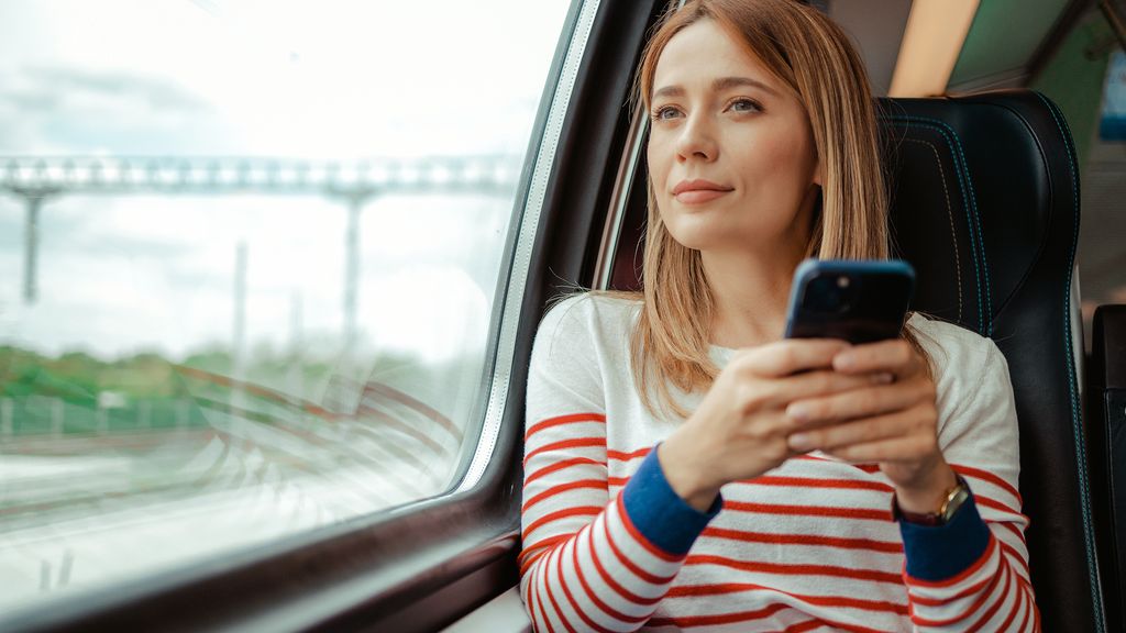 Investieren in Infrastruktur Junge Frau mit Smartphone im Zug am Fenster blickt nachdenklich nach draußen
