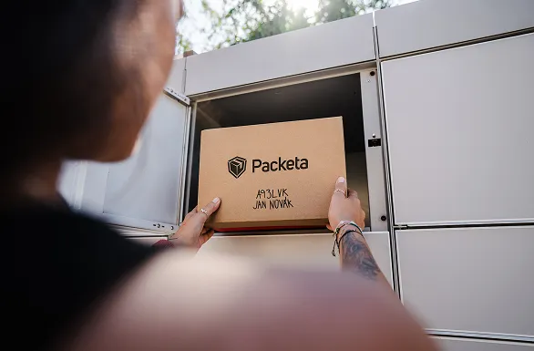 A person places a "Packeta" package labeled "A33LJK JAN NOVAK" into a locker compartment with an open door.