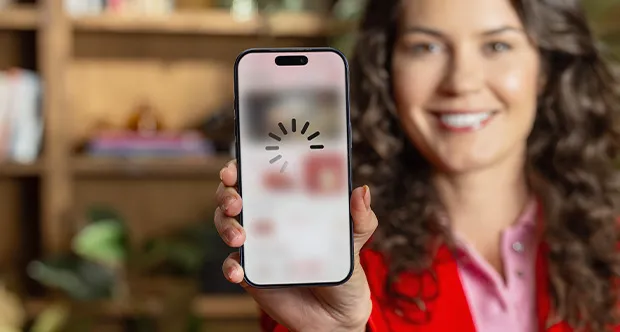 A person holding a smartphone with a loading symbol on the screen, standing in front of a wooden bookshelf.
