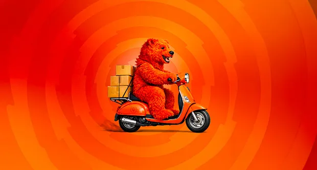 Medvěd Grizly na oranžovém skútru s balíky na zádech