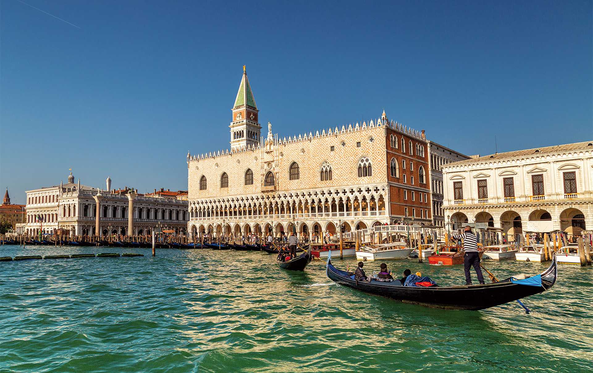 Gondolier by the Doge's Palace near St Mark's Campanile, the bell tower of St Mark's Basilica in Venice, Italy,