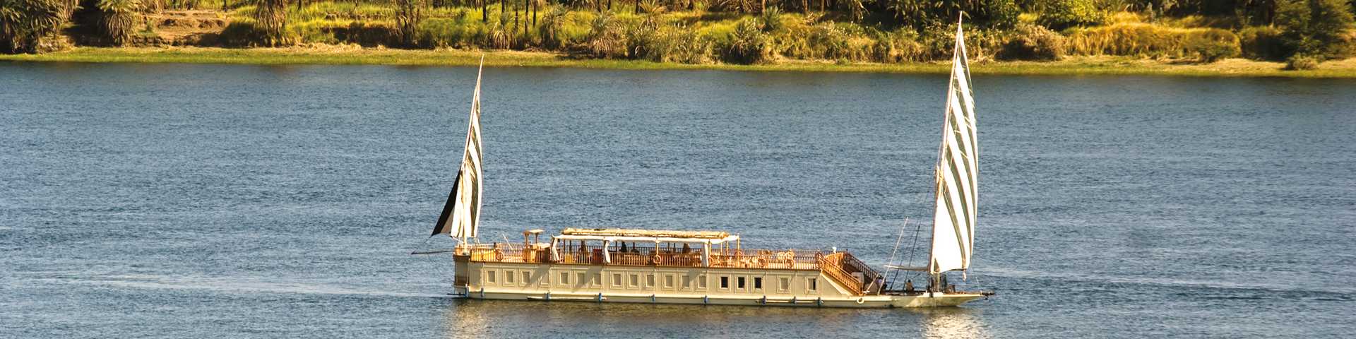 Powered by two sails, Queen Farida dahabiya travels at a leisurely pace, allowing plenty of time to soak up the changing scenery. The dahabiya’s small size and 1:1 crew to guest ratio make for an intimate, personal feel on board. En-suite cabins are comfortable and air-conditioned, with dark-wood furniture, handmade salt lamps, parquet flooring and windows looking out to the water. Upgrade to a suite and you’ll have a private balcony. 
Relax in the cool comfort of the lounge or choose a spot up on deck – comfy cushions are laid out beneath the canopy, while parasol-shaded loungers face the water. Meals are usually taken up here. They’re à la carte and often several courses long, with a focus on traditional Egyptian cuisine.