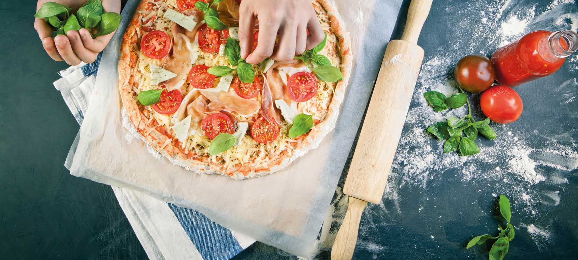 A chef adds fresh basil to a pizza