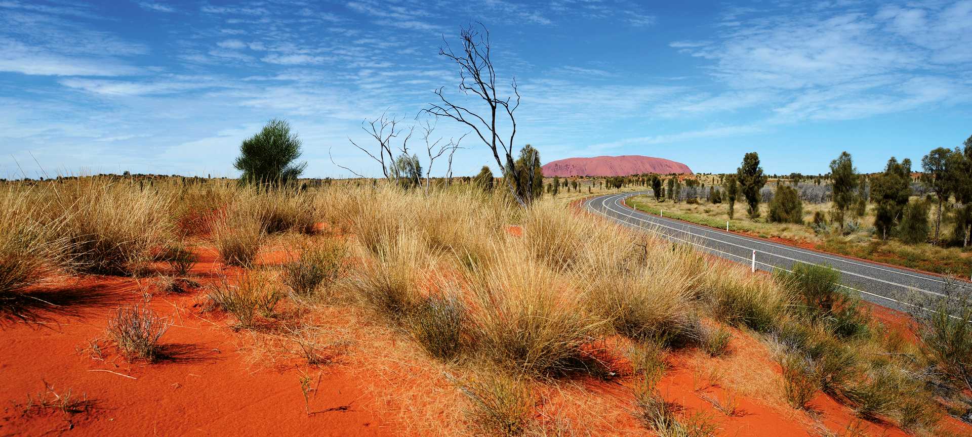 Road through red rocky landscape to Uluru, Australia