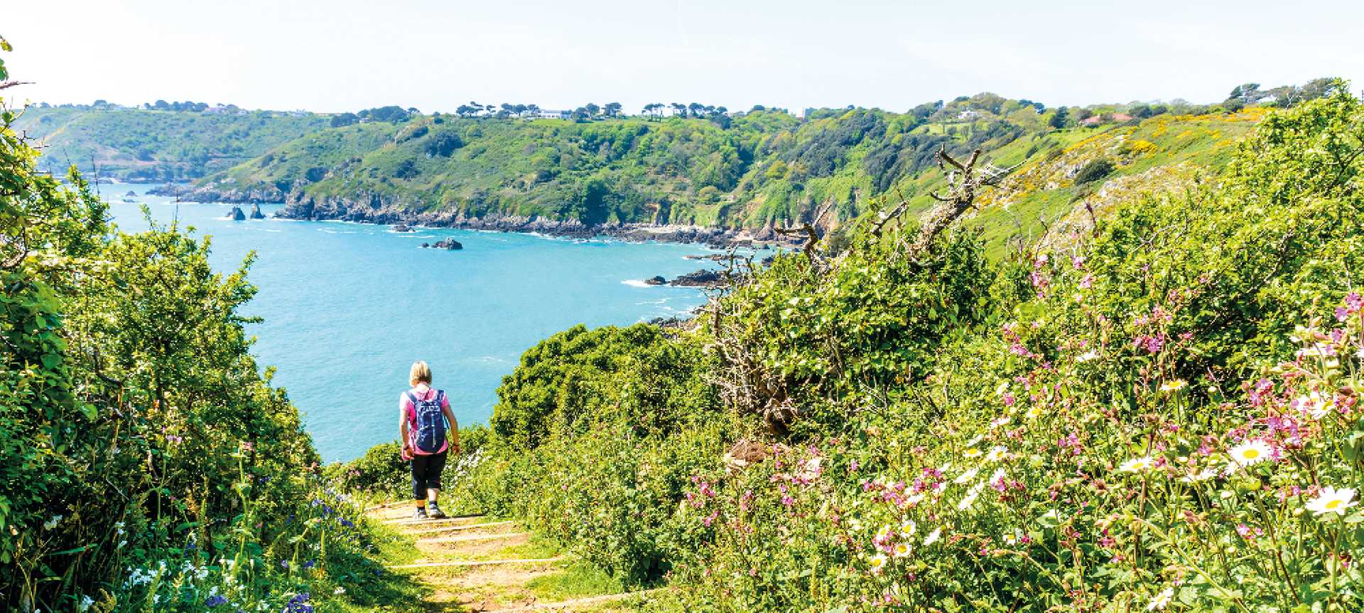 A walker heads down a coastal path towards the sea