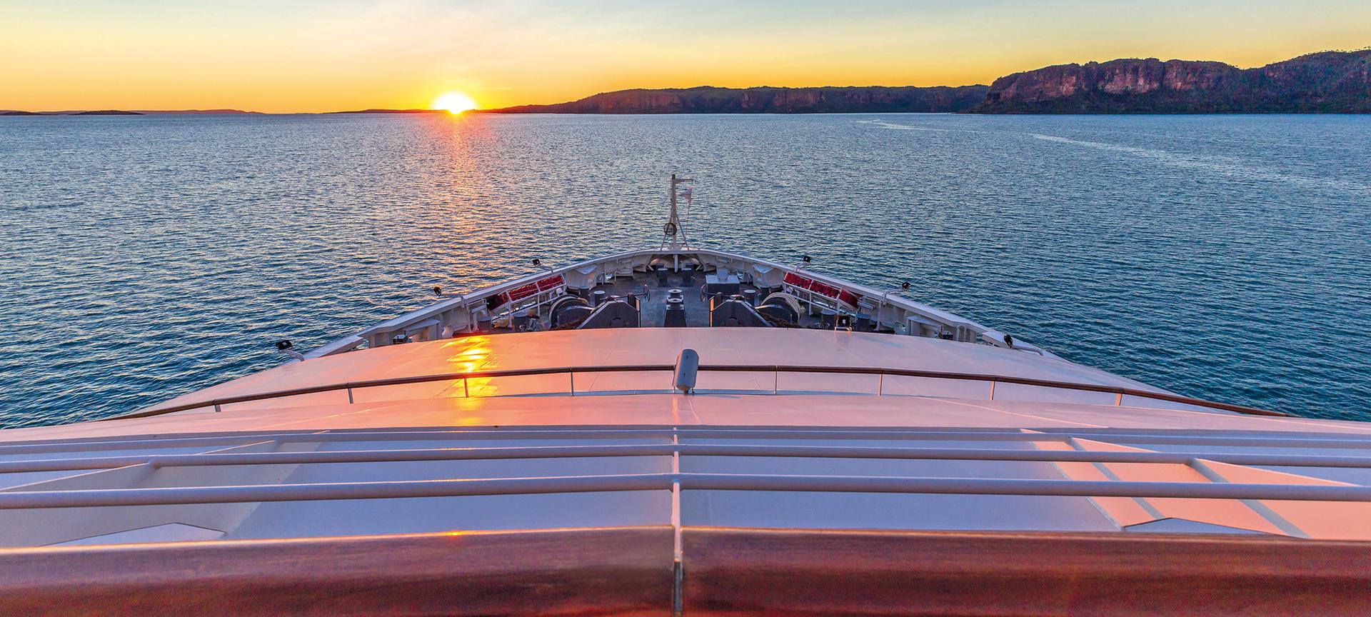 Bow of cruise ship sailing towards sunset