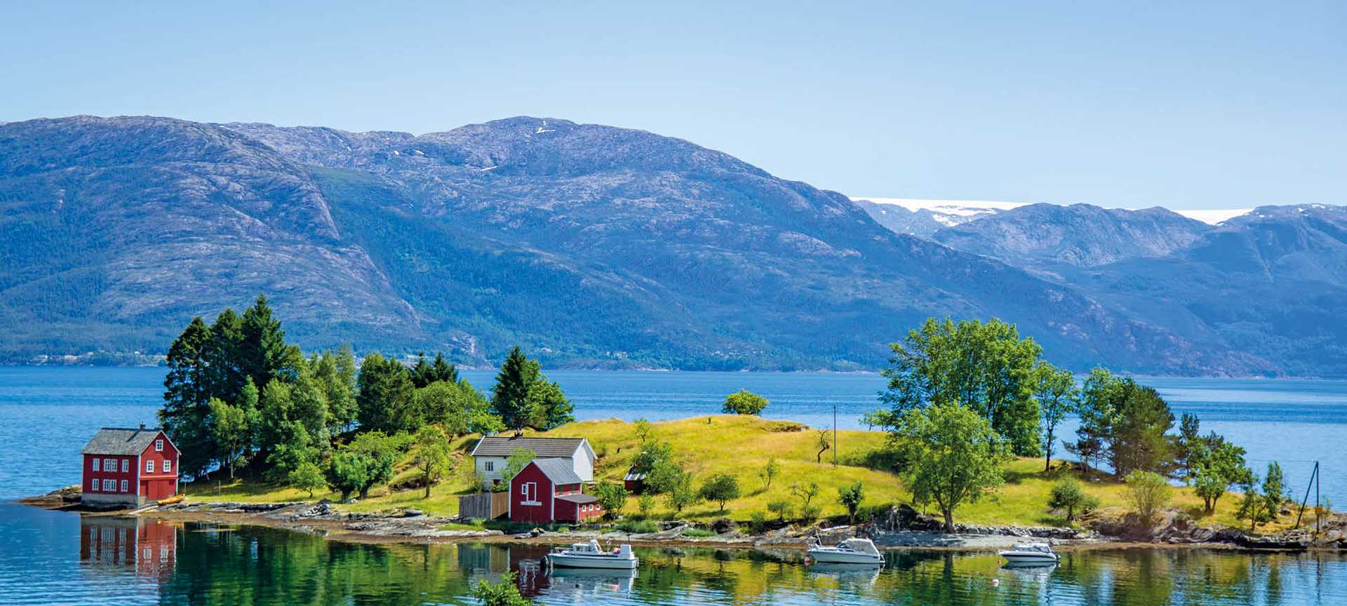 Red wooden houses sit on a small island in Hardangerfjord, Norway