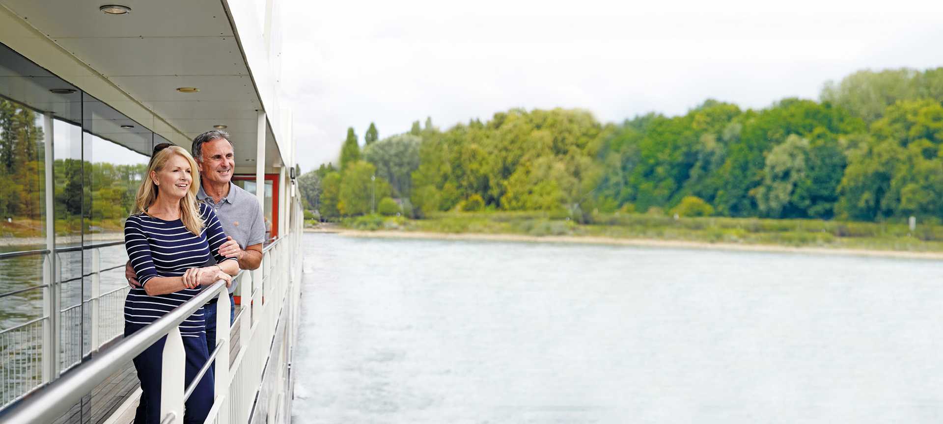 Couple stand on deck of a river cruise ship watching the scenery go by