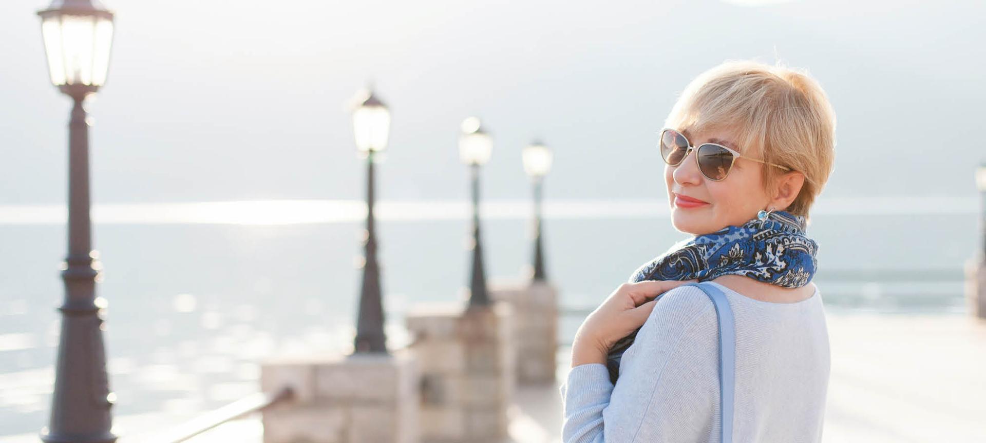 A solo traveller in a scarf and sunglasses smiles at the camera