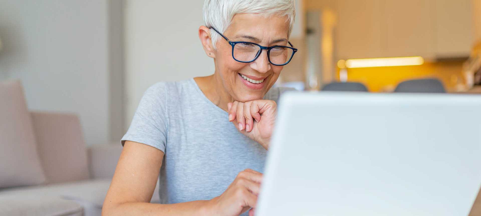 A woman smiles and sits in front of a white laptop