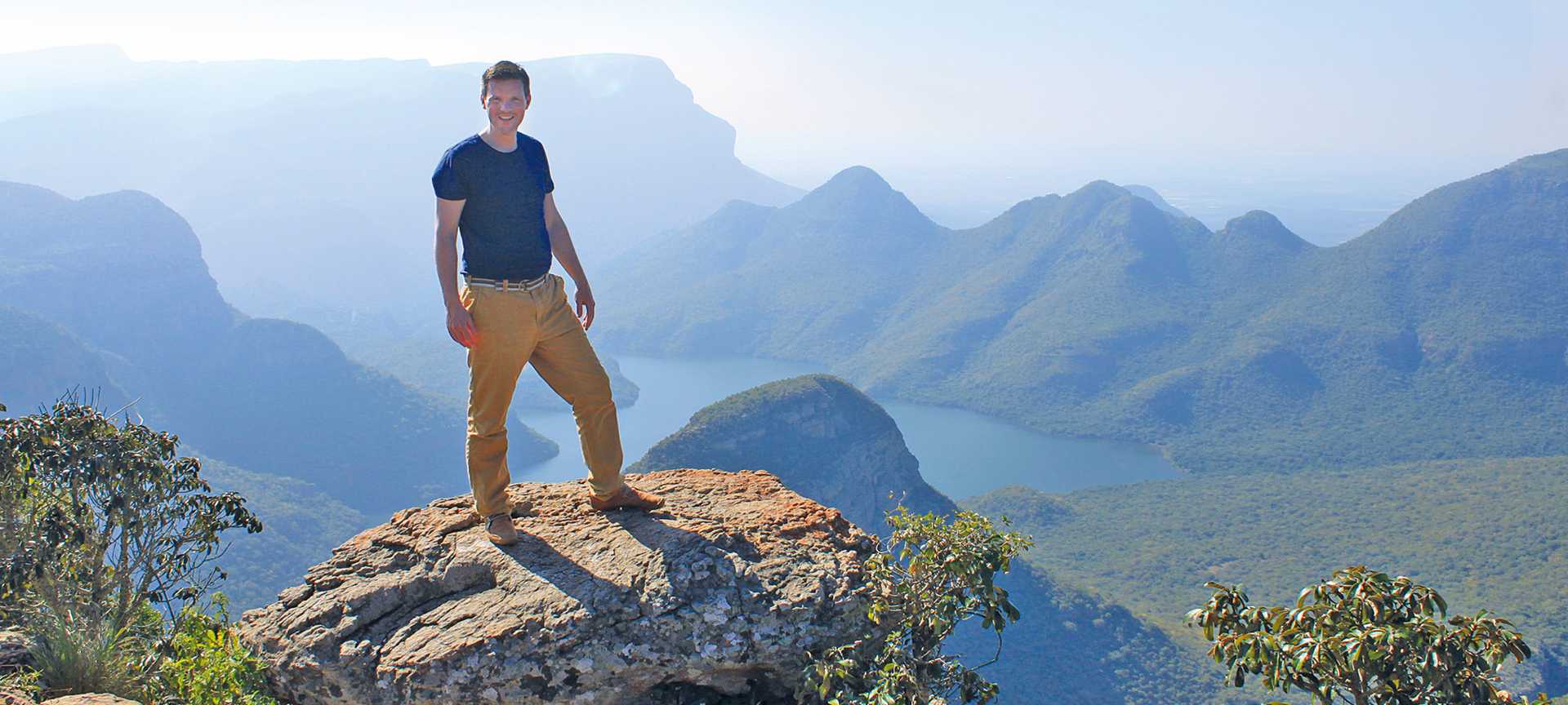 Titan Product manager Phil Ellis stands on top of a rock with lake views behind, South Africa