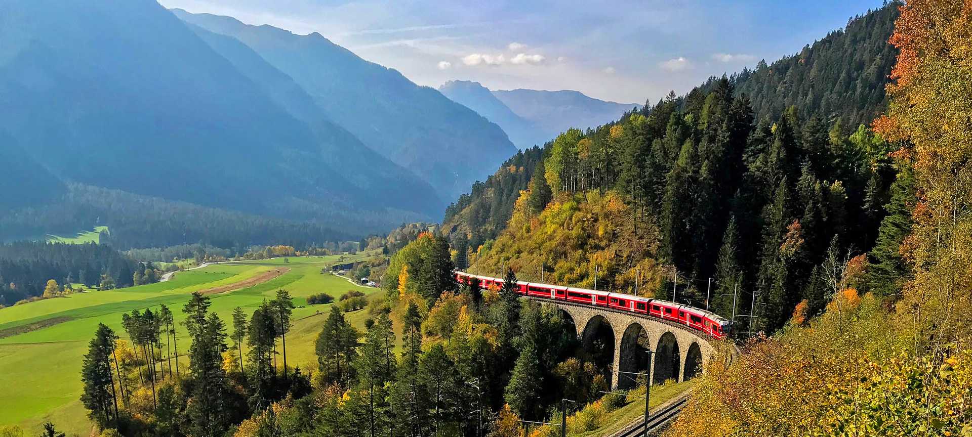 The Bernina Express travels over a viaduct in Switzerland, with mountains behind