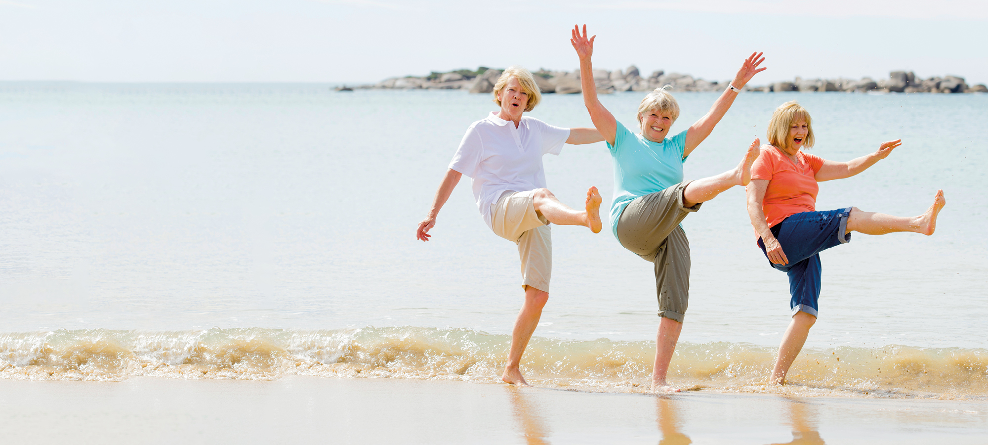 Three friends dance in the shallows while visiting a beach
