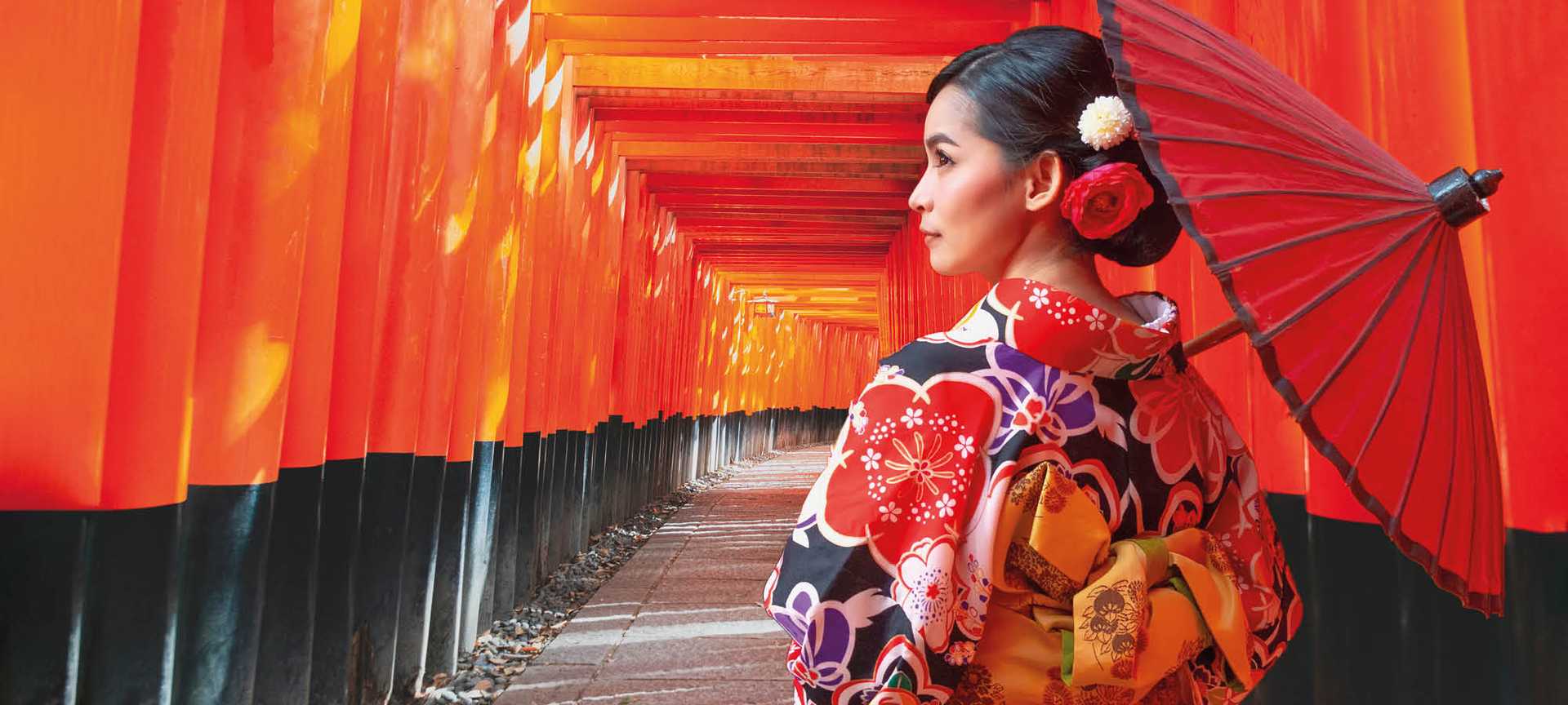 A woman in a traditional kimono holds a parasol at Fushimi Inari Shrine in Kyoto, Japan