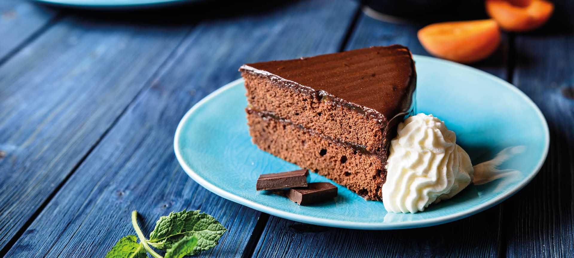 A slice of sachertorte with cream served on a blue plate