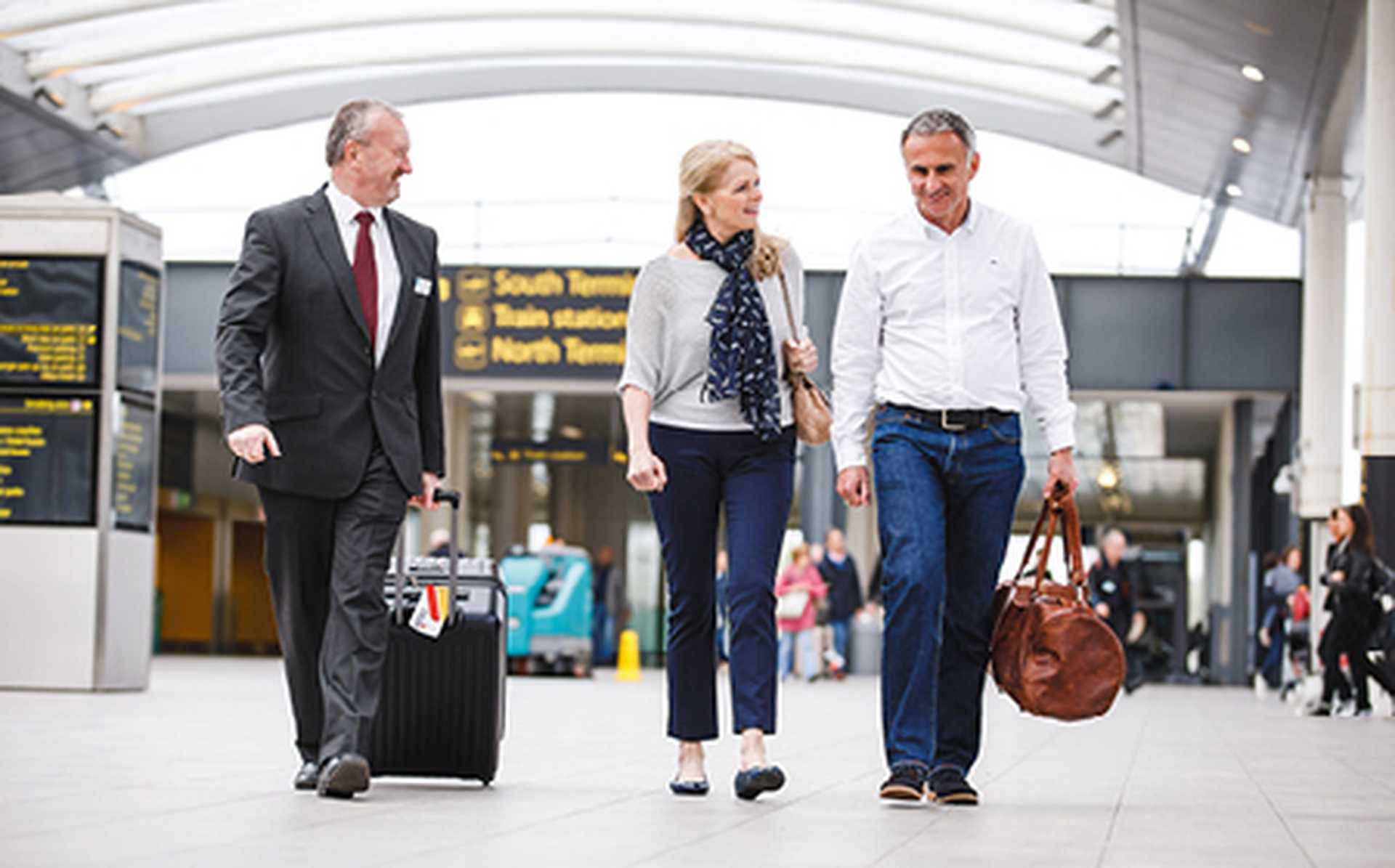 A man and woman are walking through the airport terminal. They are smiling. Titan's Airport Representative is helping them with their suitcase. 
