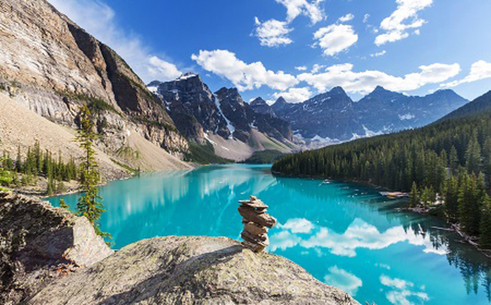View across the turquoise waters of Moraine Lake, edged with thick forest and towering peaks. Visit Banff National Park on Titan's Canadian Rockies tours