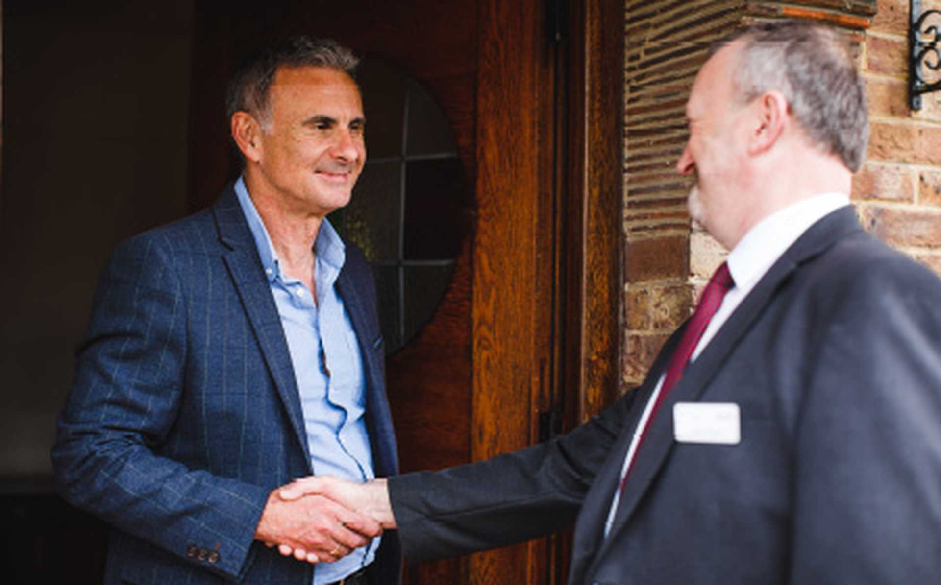 Titan VIP door-to-door transfer service chauffeur shakes hand with customer at their front door.