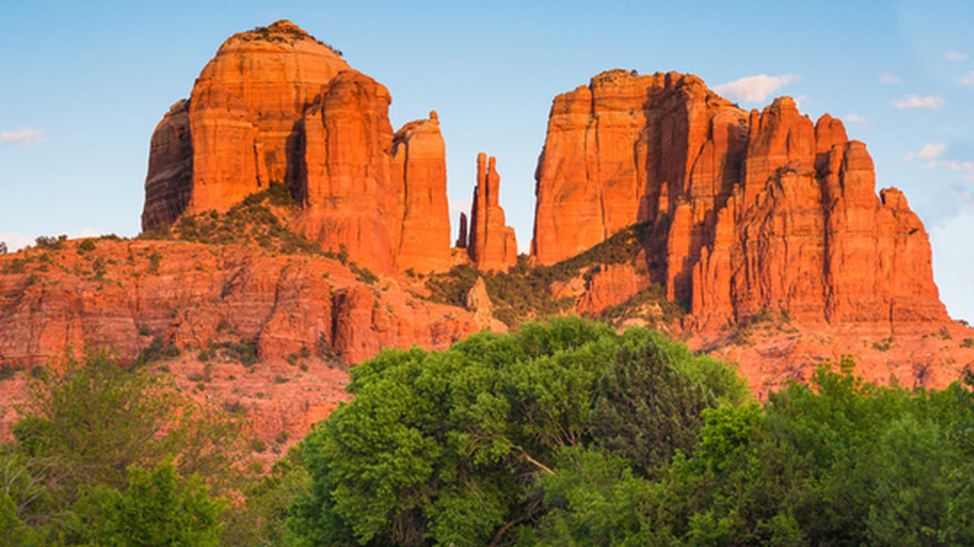 Cathedral Rock sandstone formation stands against a blue sky with green trees in the foreground. Taken in Coconino National Forest, Yavapai Country, Arizona, United States.