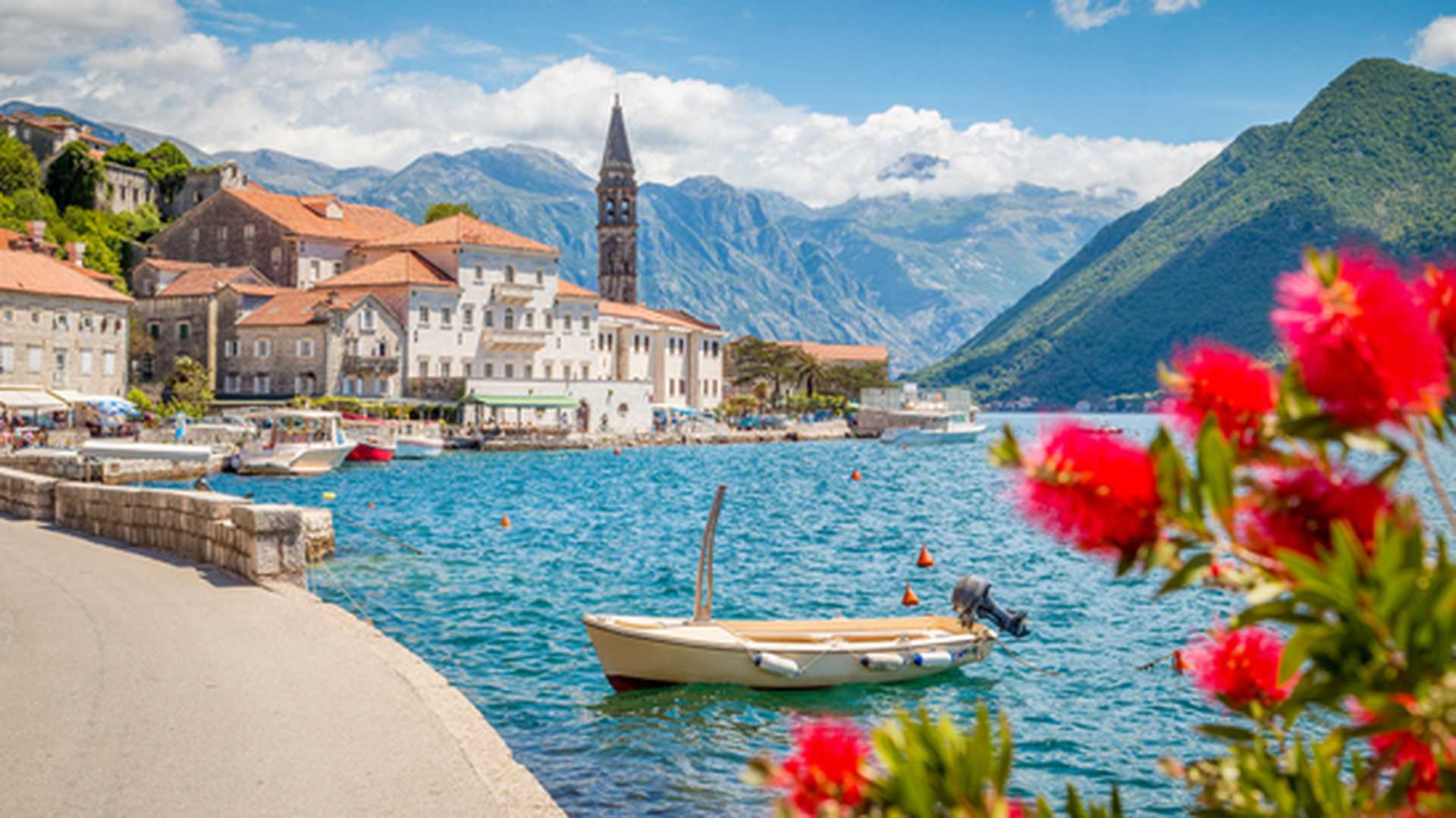Scenic panorama view of the historic town of Perast at famous Bay of Kotor with blooming flowers on a beautiful sunny day with blue sky and clouds in summer, Montenegro, southern Europe