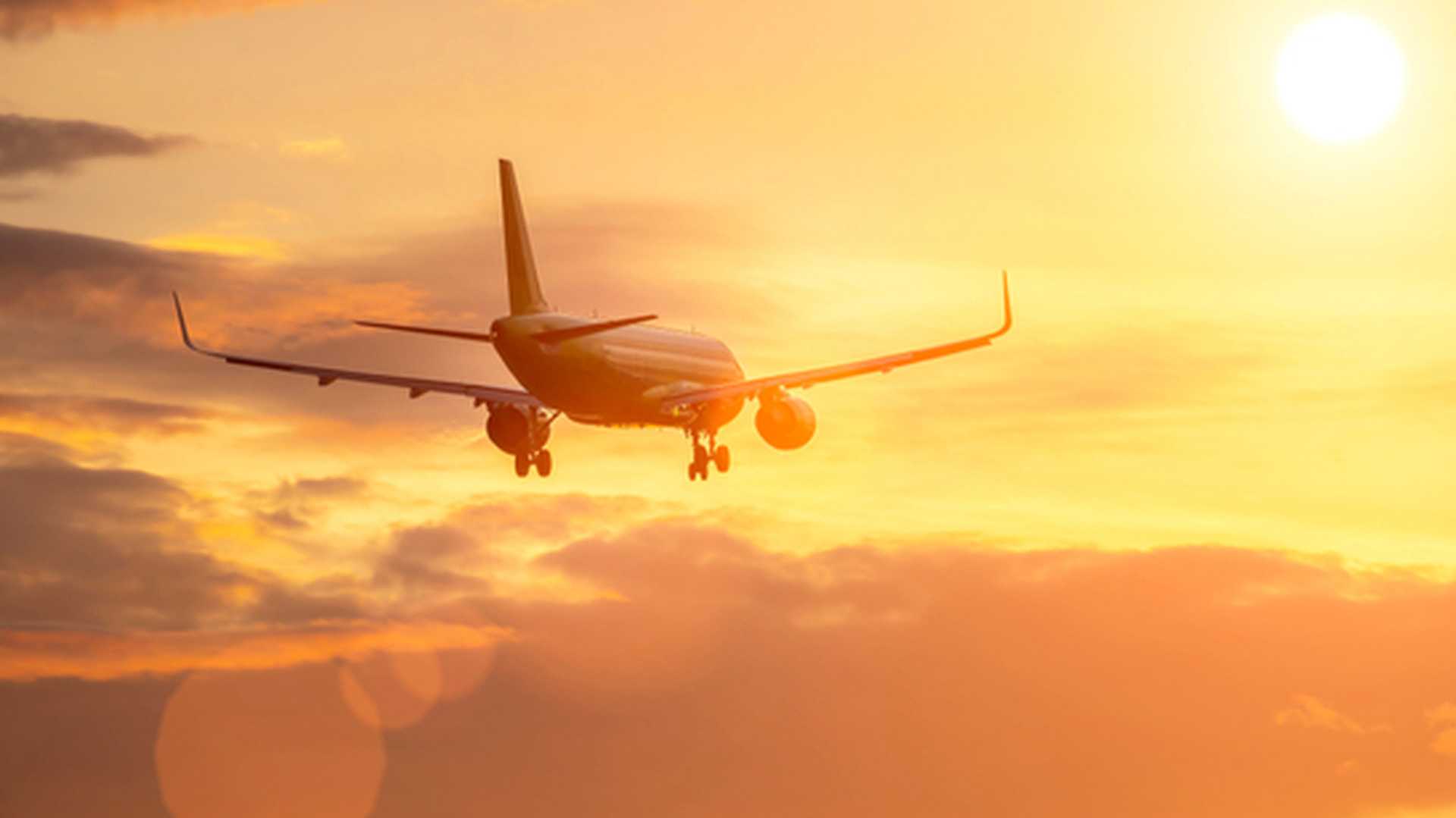 plane flies in sky towards sun.