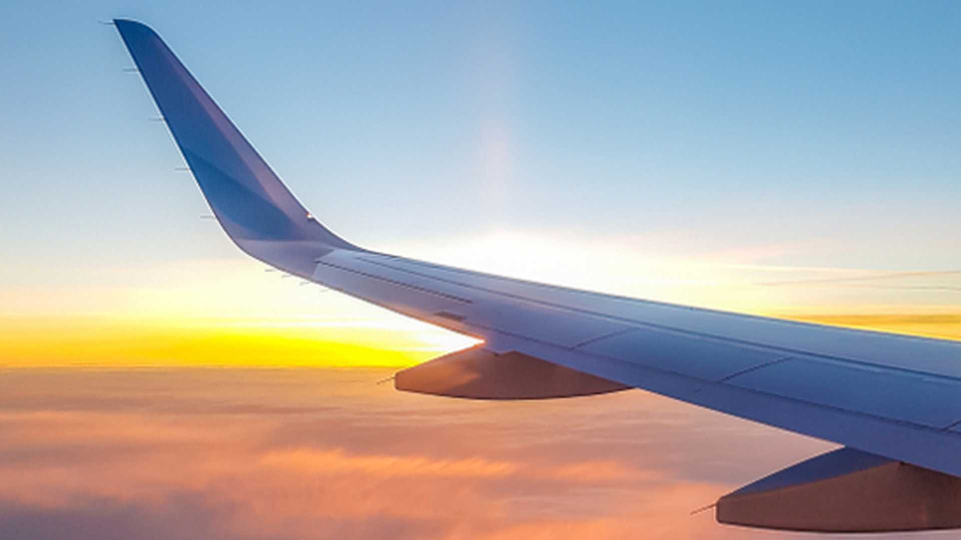 Wing of a plane in flight looking down on clouds