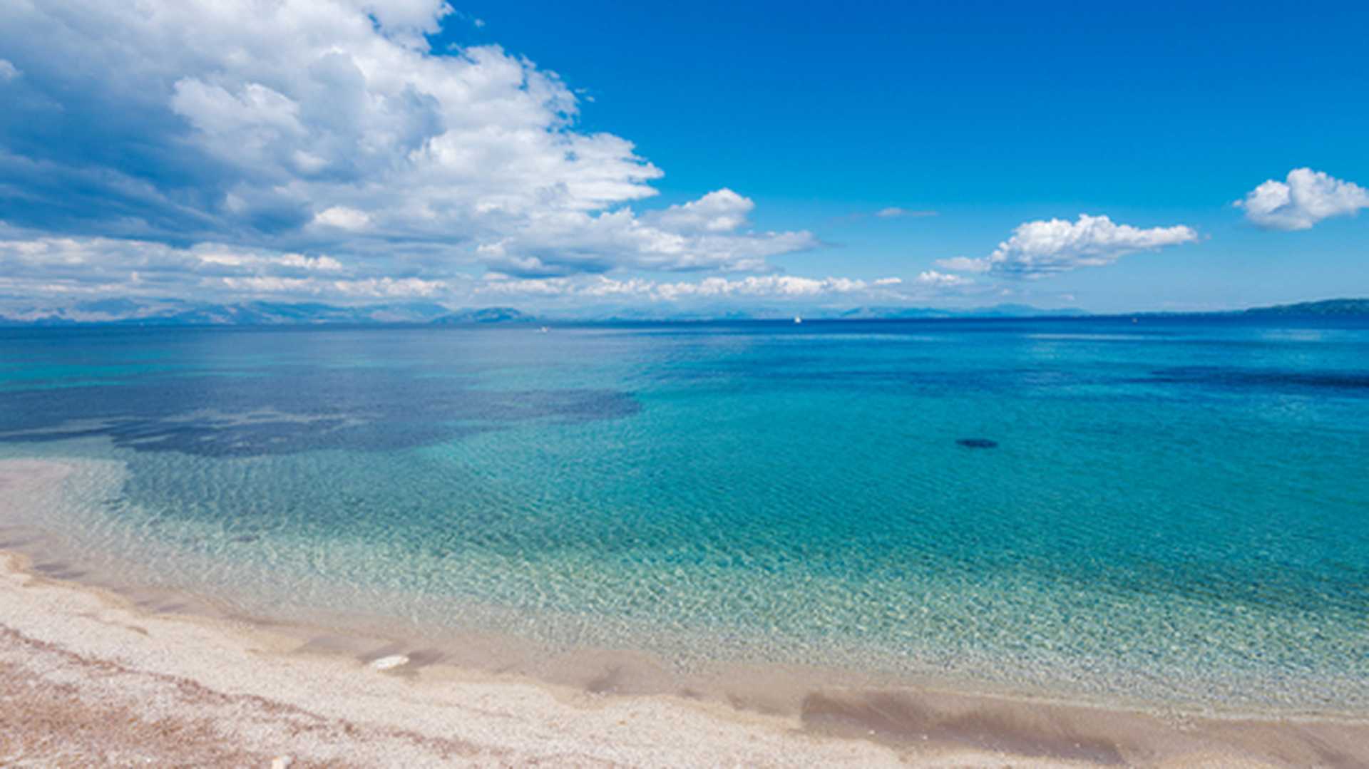 Looking out across clear, turquoise waters from Agios Ioannis Peristeron beach in Corfu, Greece