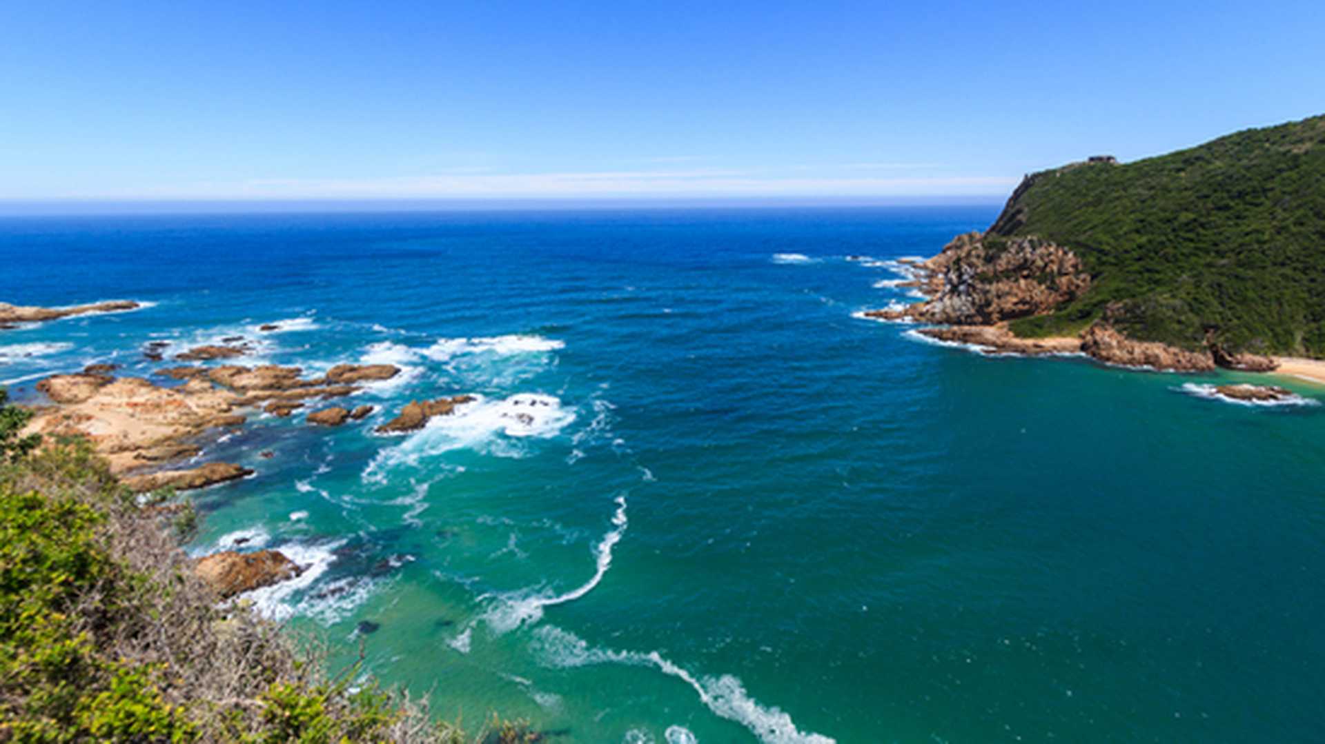 Forested cliffs and rocky promontories lead down to turquoise waters at Knysa Heads, visited on Titan's Best of South Africa tours