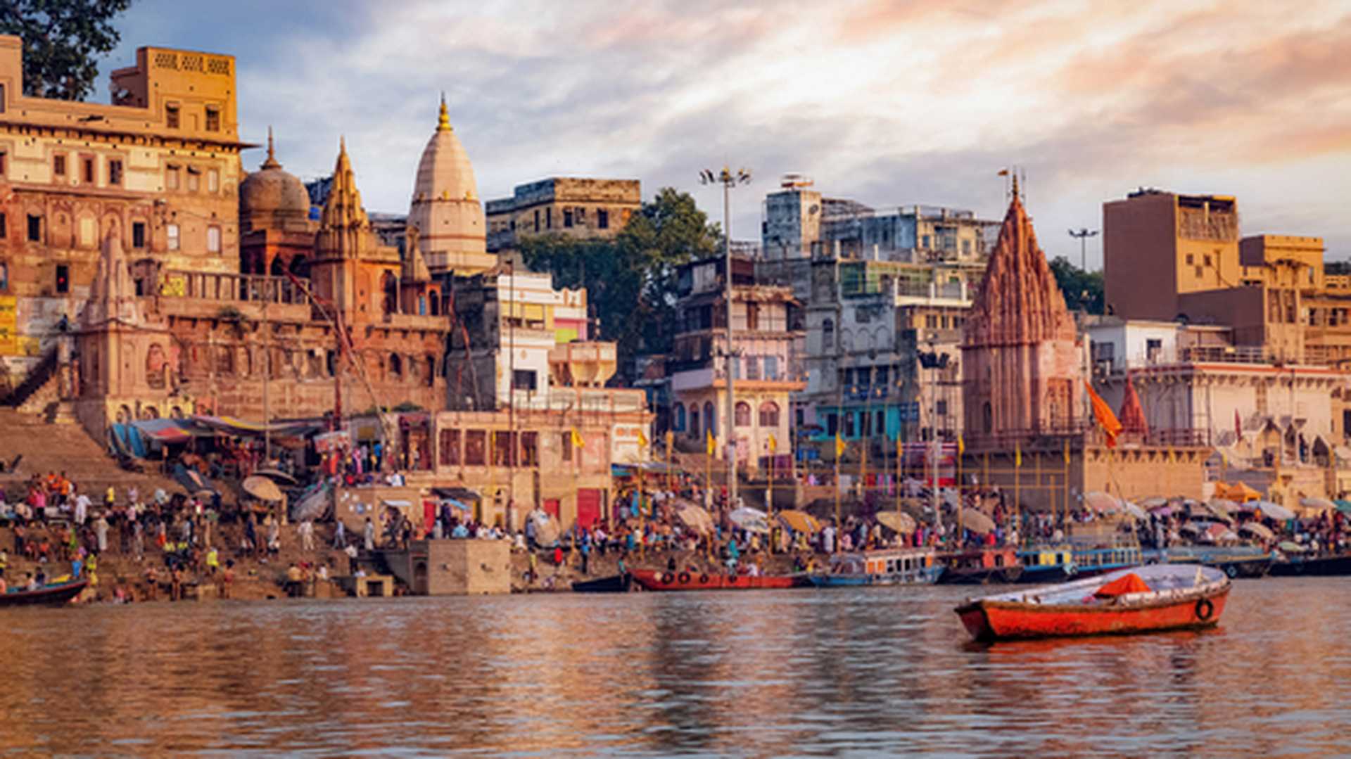 Historic Varanasi city with ancient temples and buildings along the Ganges river ghat as viewed from a boat at sunrise.