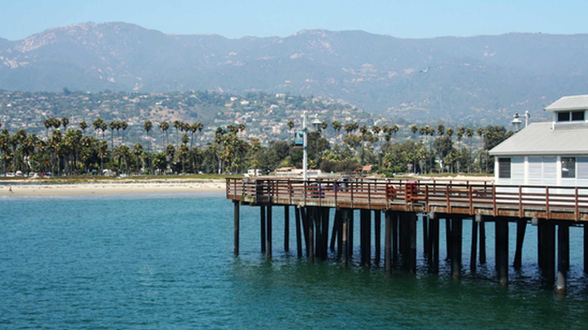 The pier at Santa Barbara, looking back towards a palm-lined sandy beach and mountains behind, California
