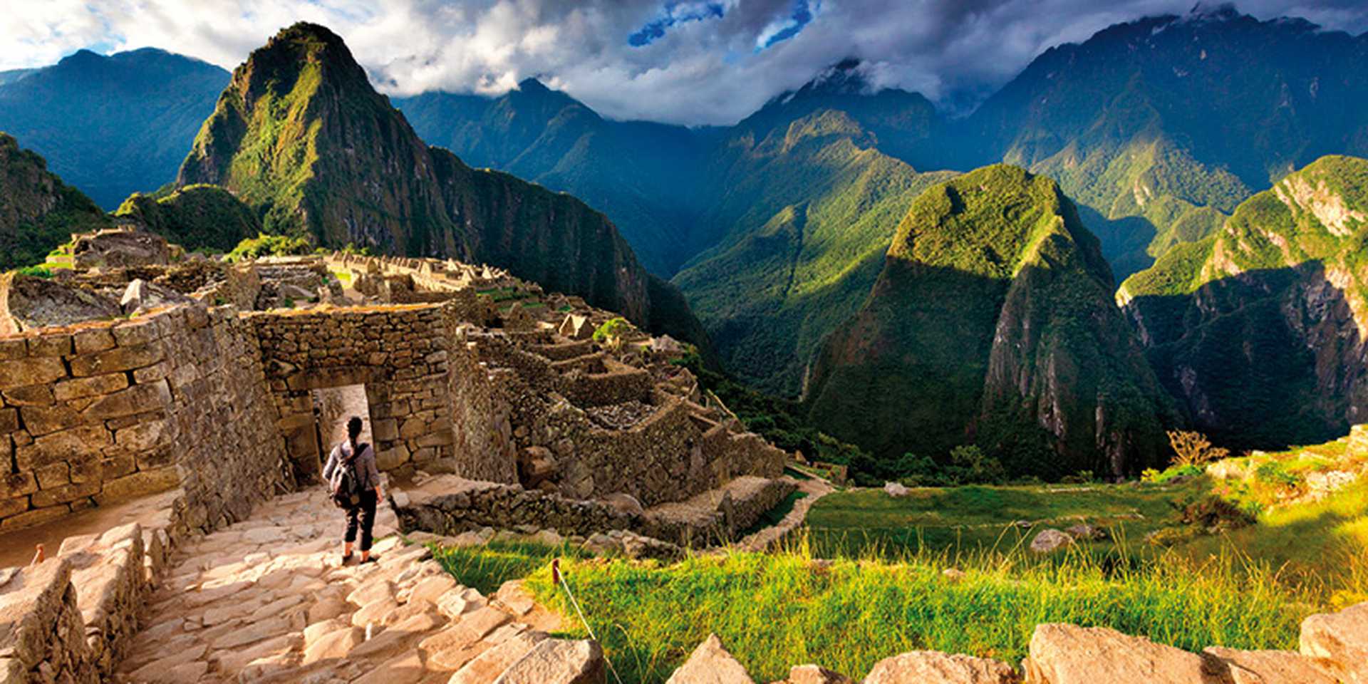 Back view of female tourist descending stairs overlooking Machu Picchu ruins at sunset, Peru
