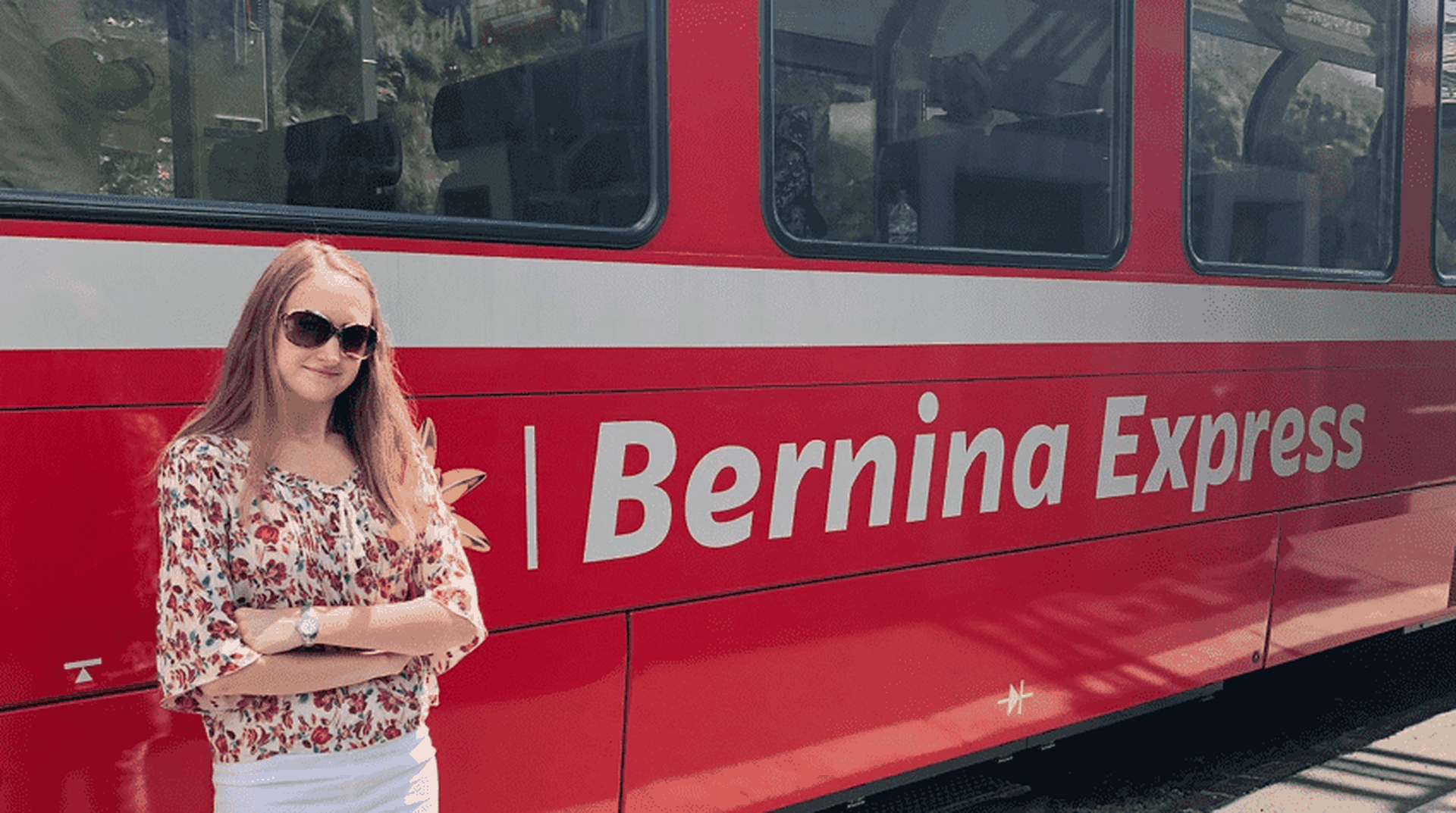 Harriet stands next to the red carriages of the Bernina Express in Switzerland