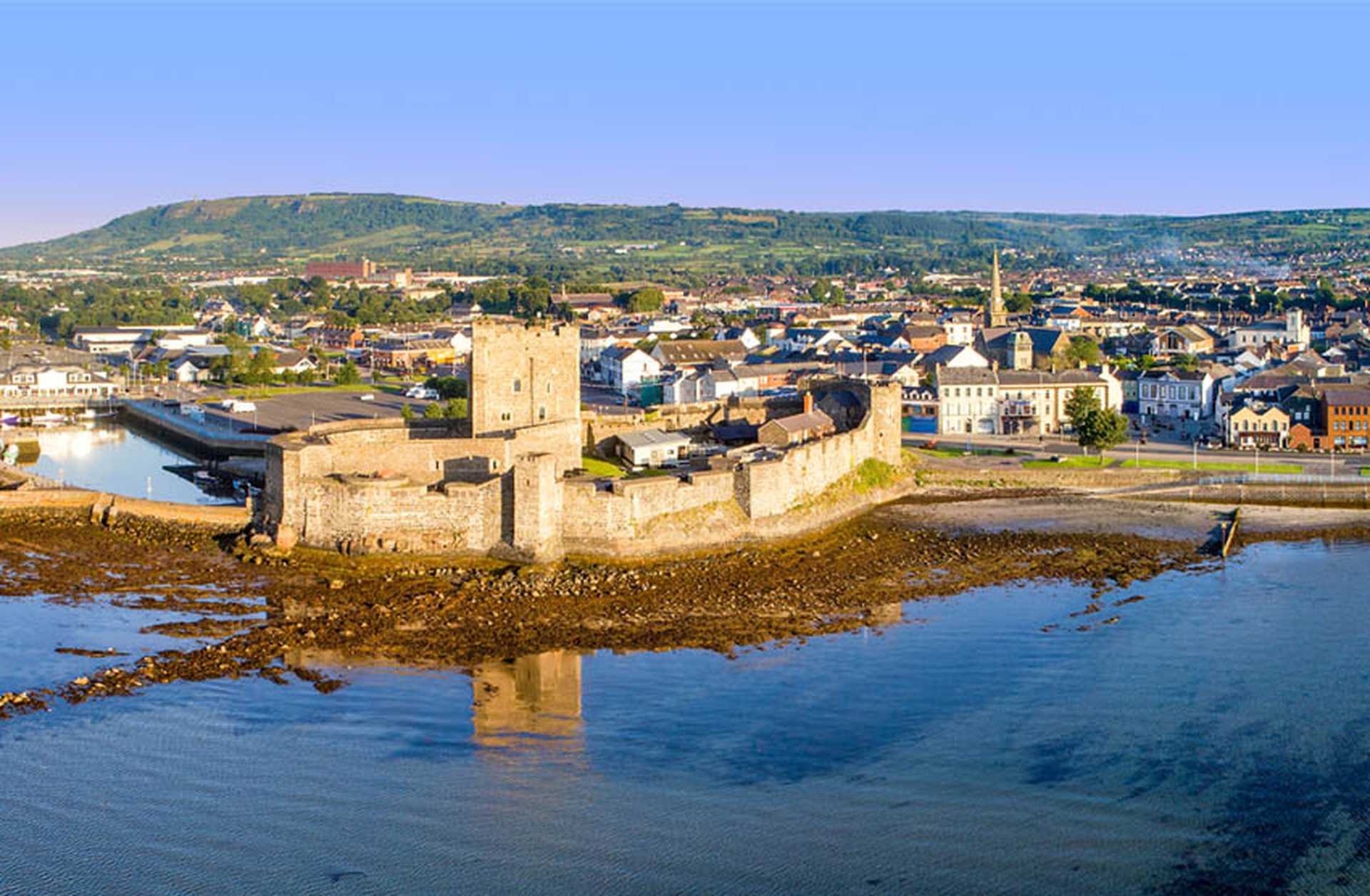 Medieval Norman castle in Carrickfergus near Belfast, with marina, town, Belfast Lough and far view of Belfast city in the background