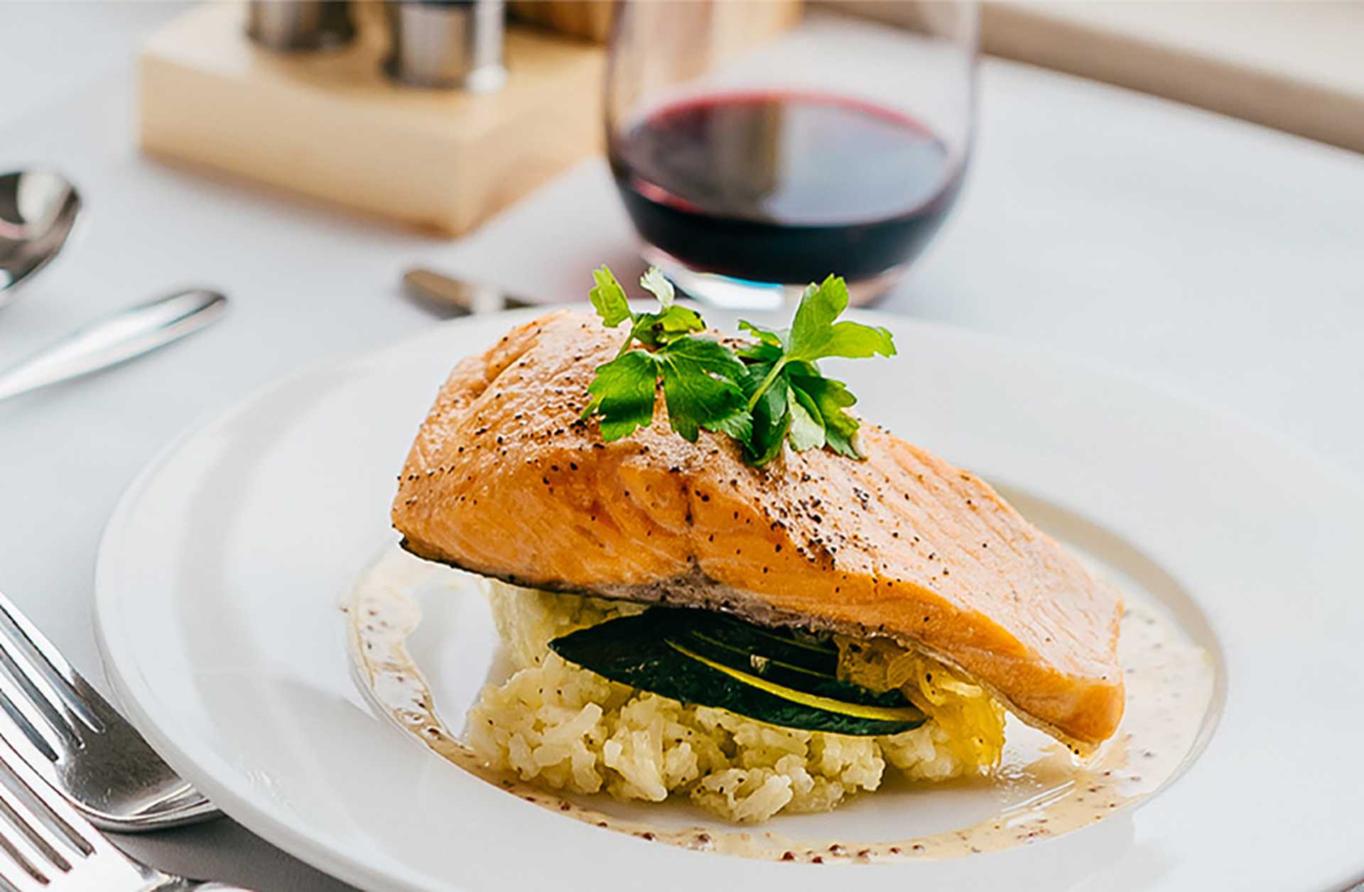 Sockeye salmon served on a white plate beside a glass of red wine. Recipe from Rocky Mountaineer