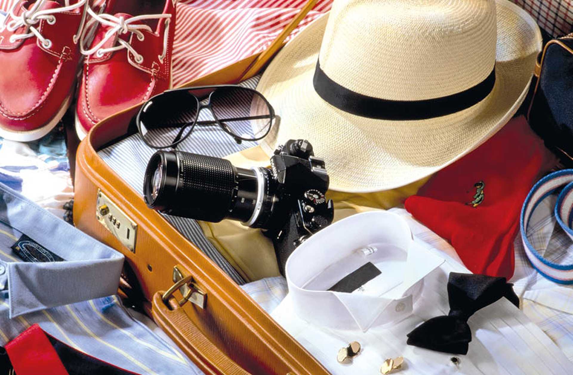 A suitcase is packed for a holiday with camera, hat, sunglasses, clothes and shoes