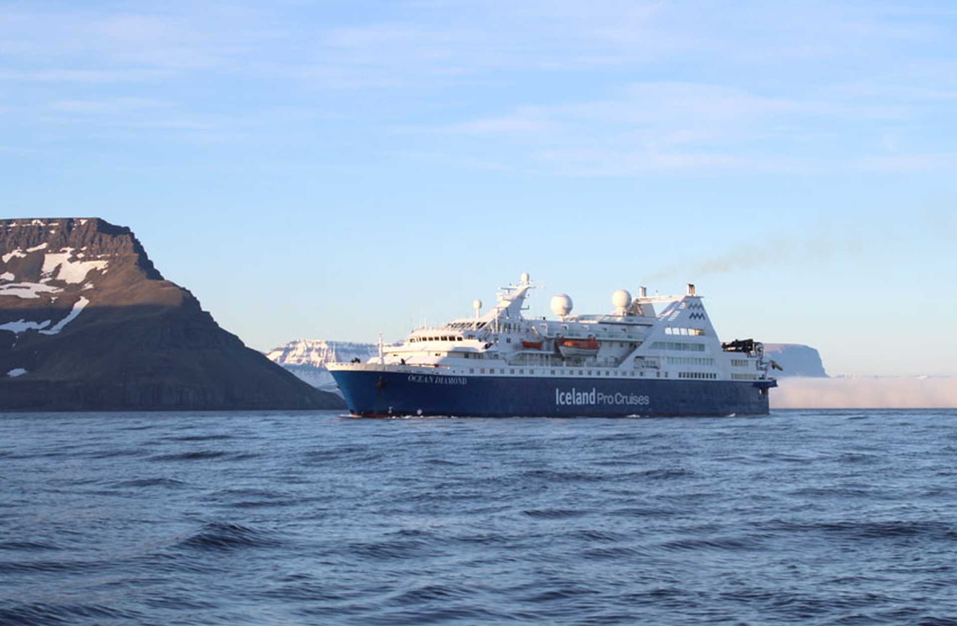 Ocean Diamond expedition cruise ship sails along Iceland's beautiful Westfjords, with snowy mountains in the background