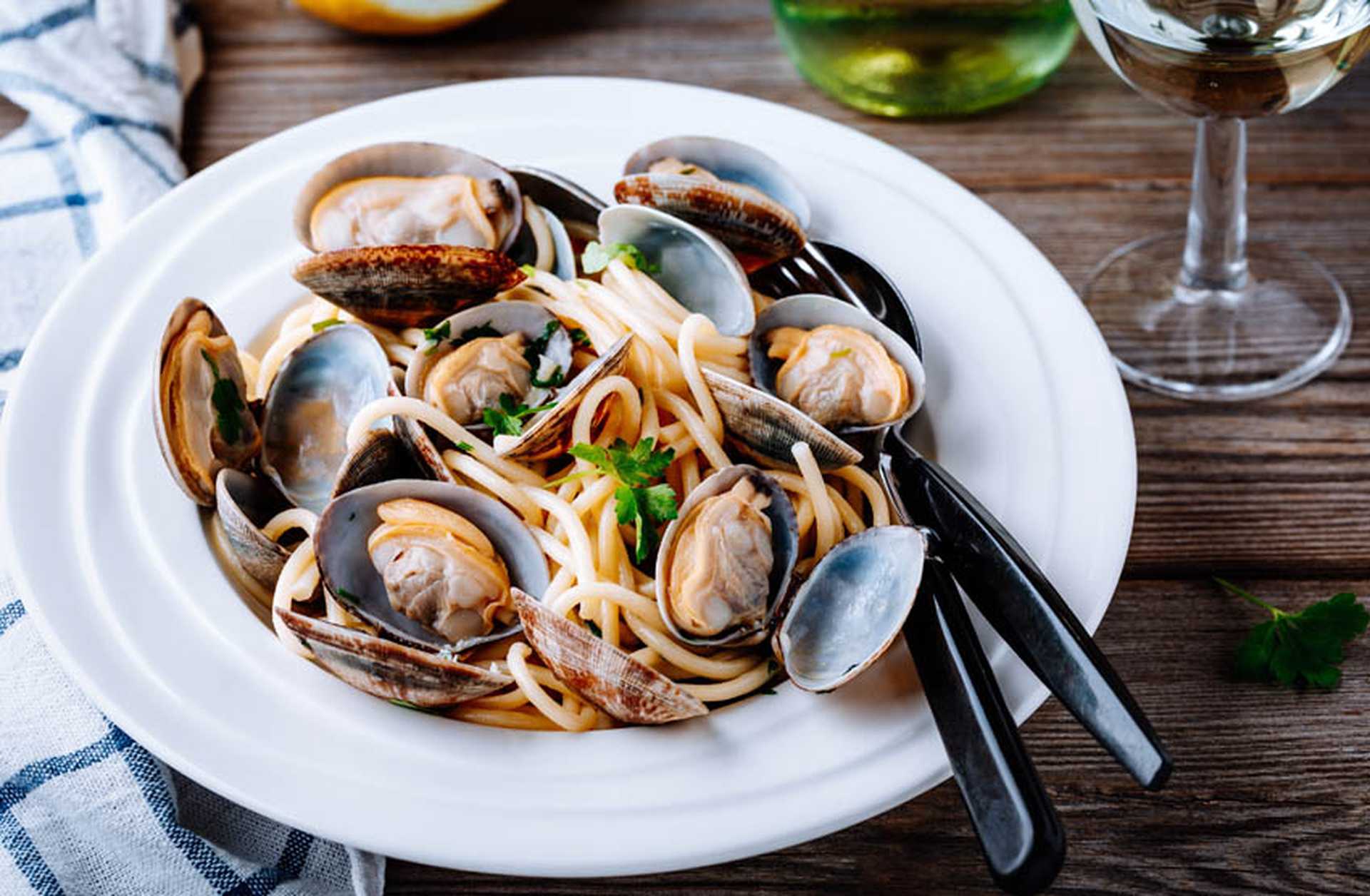 A plate of seafood pasta placed next to a glass of white wine