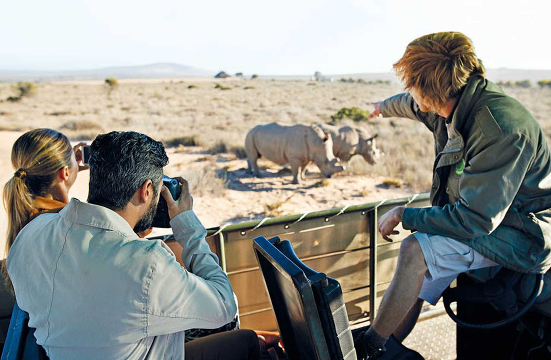 A guide points out wildlife to a couple holding cameras on a safari game drive