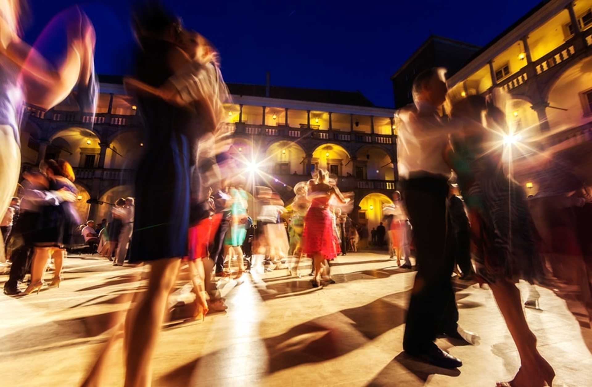 Couples dance the tango in a courtyard at night, their motion blurring the image