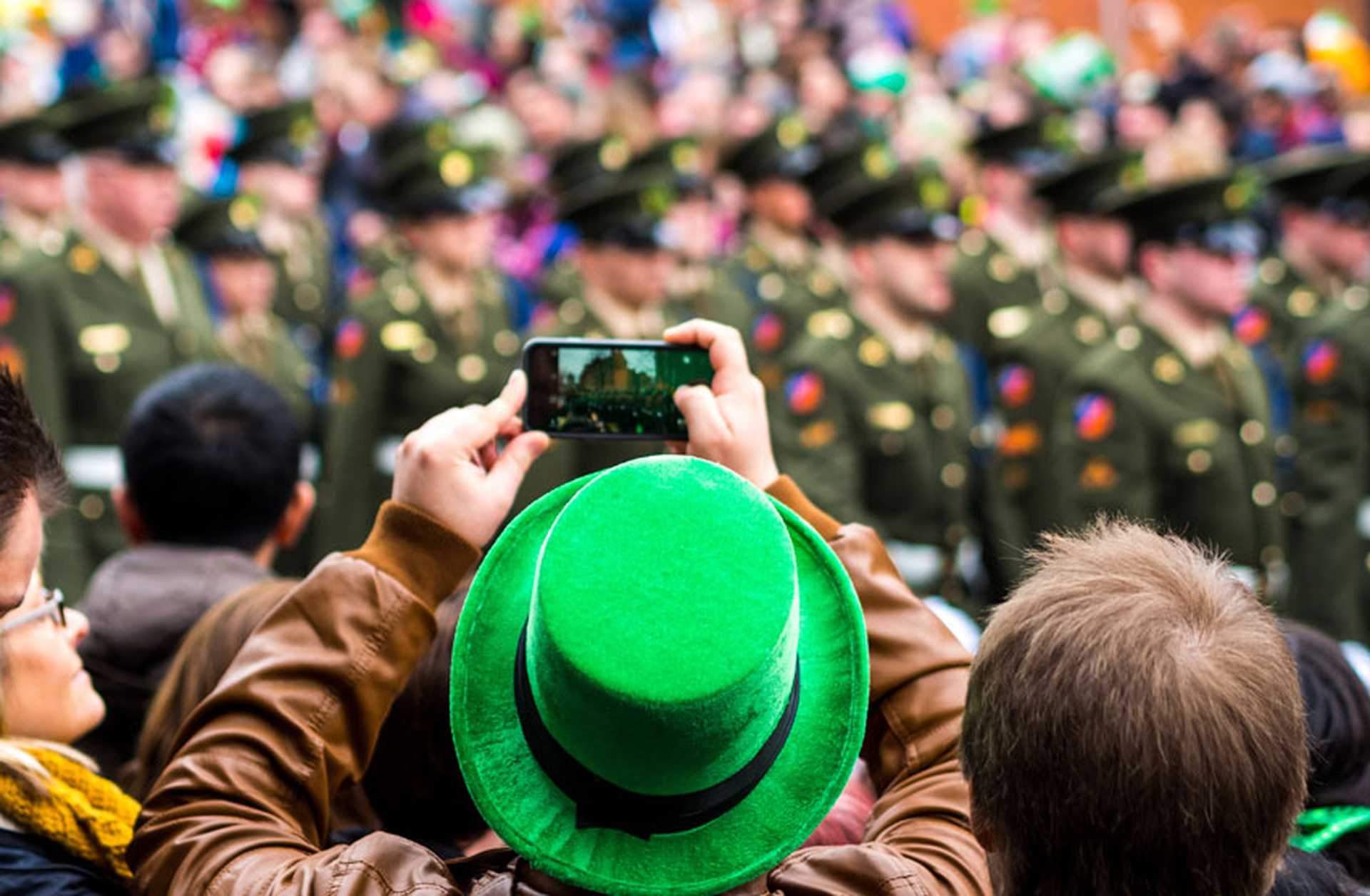 A man in a green hat photographs a St Patrick's Day parade in Dublin, Ireland