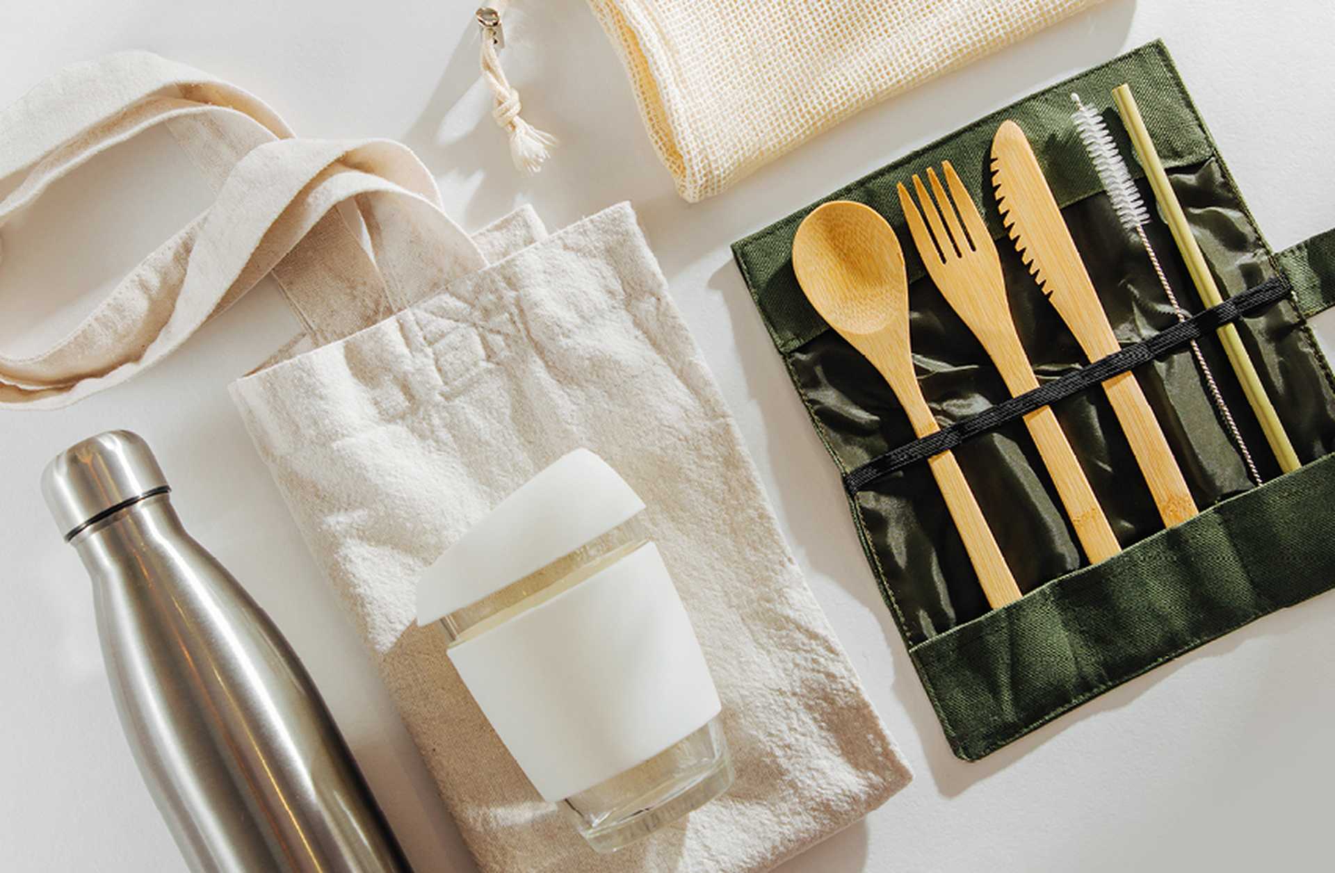 Eco-friendly travel kit: bamboo cutlery, a reusable cup and water bottle, and a canvas tote bag