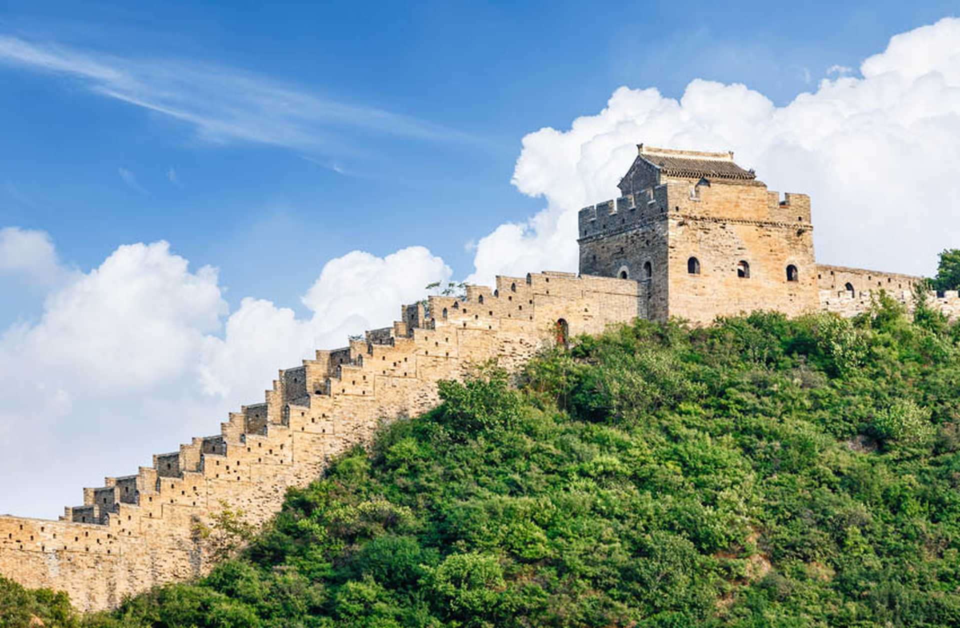A section of the Great Wall of China rises from a forested hill