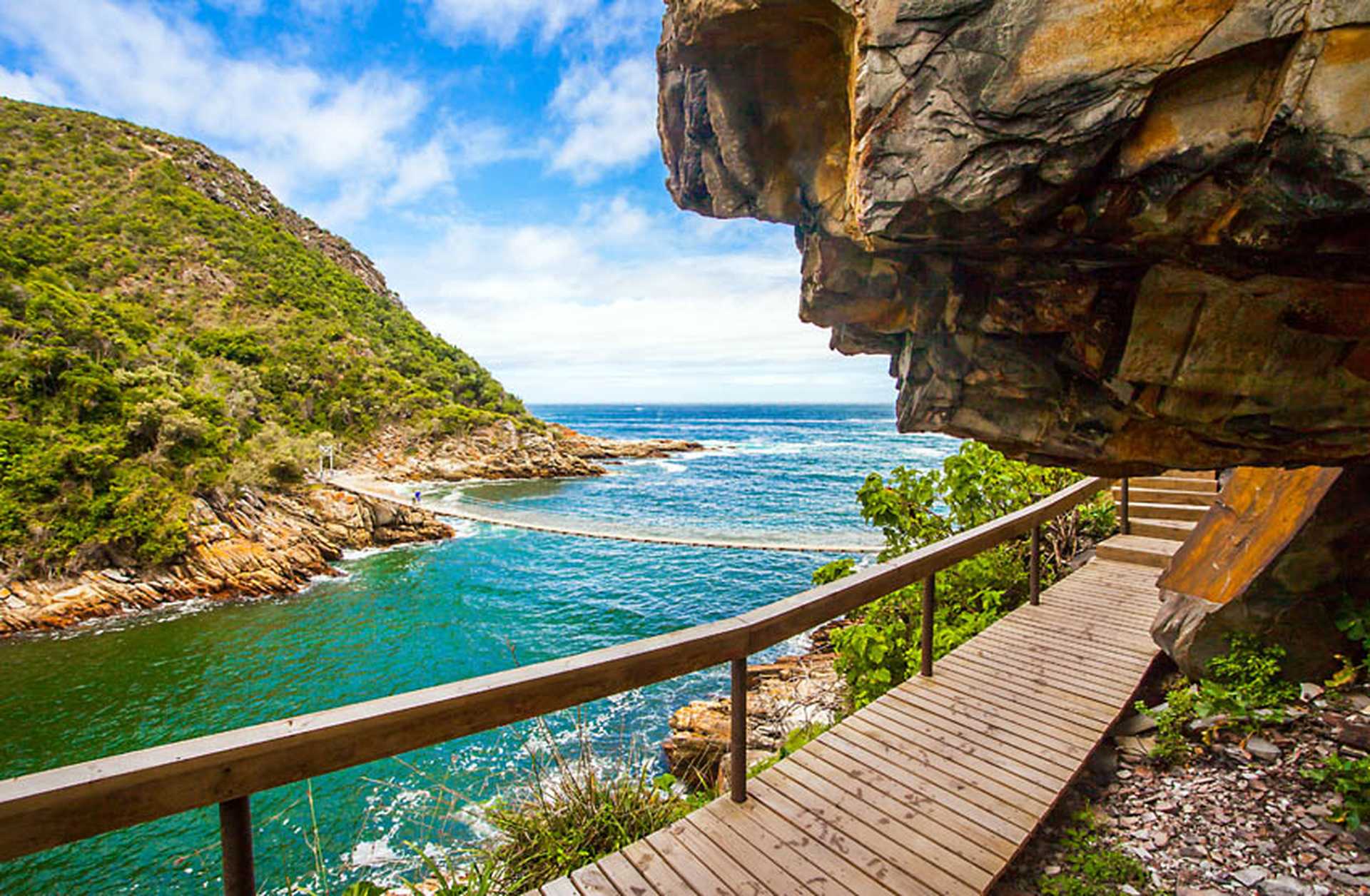 A wooden walkway leads to a bridge across the mouth of a river in Tsitsikamma National Park, South Africa