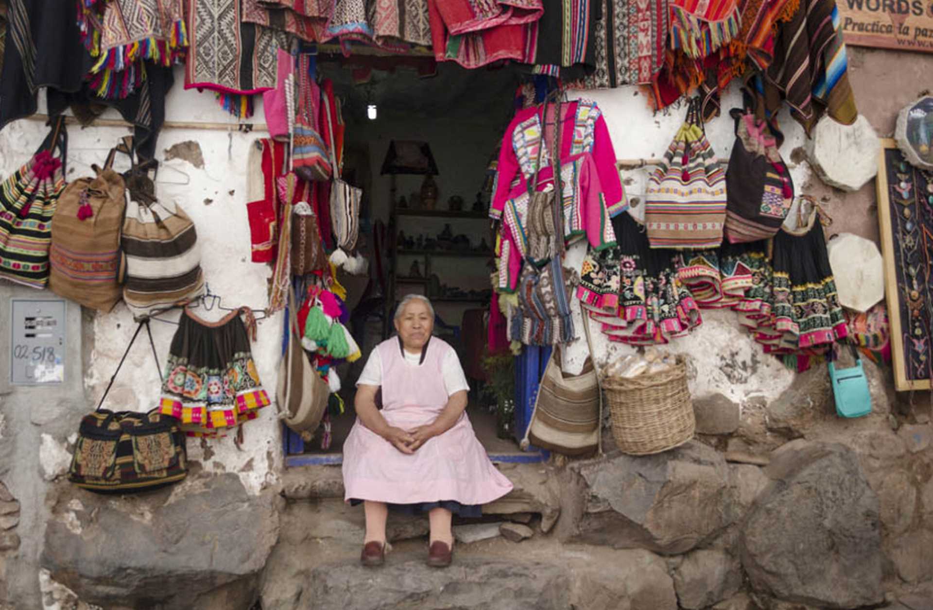 A woman sits in the doorway of a shop selling traditional Peruvian crafts