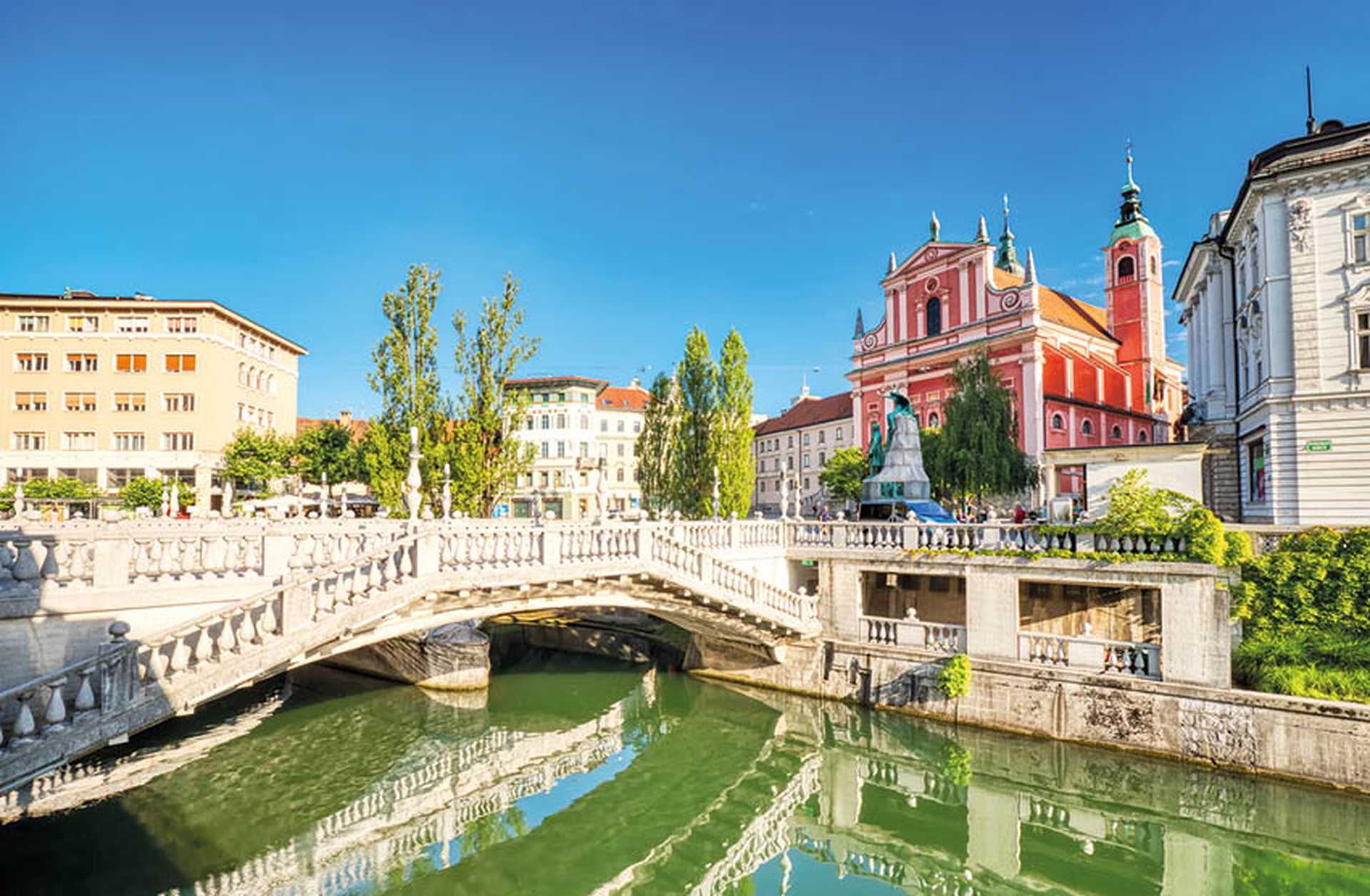 Looking across the Ljubljanica River to the Triple Bridge and pink facade of the Franciscan Church of the Annunciation in Ljubljana, visited on Titan's Slovenia tours