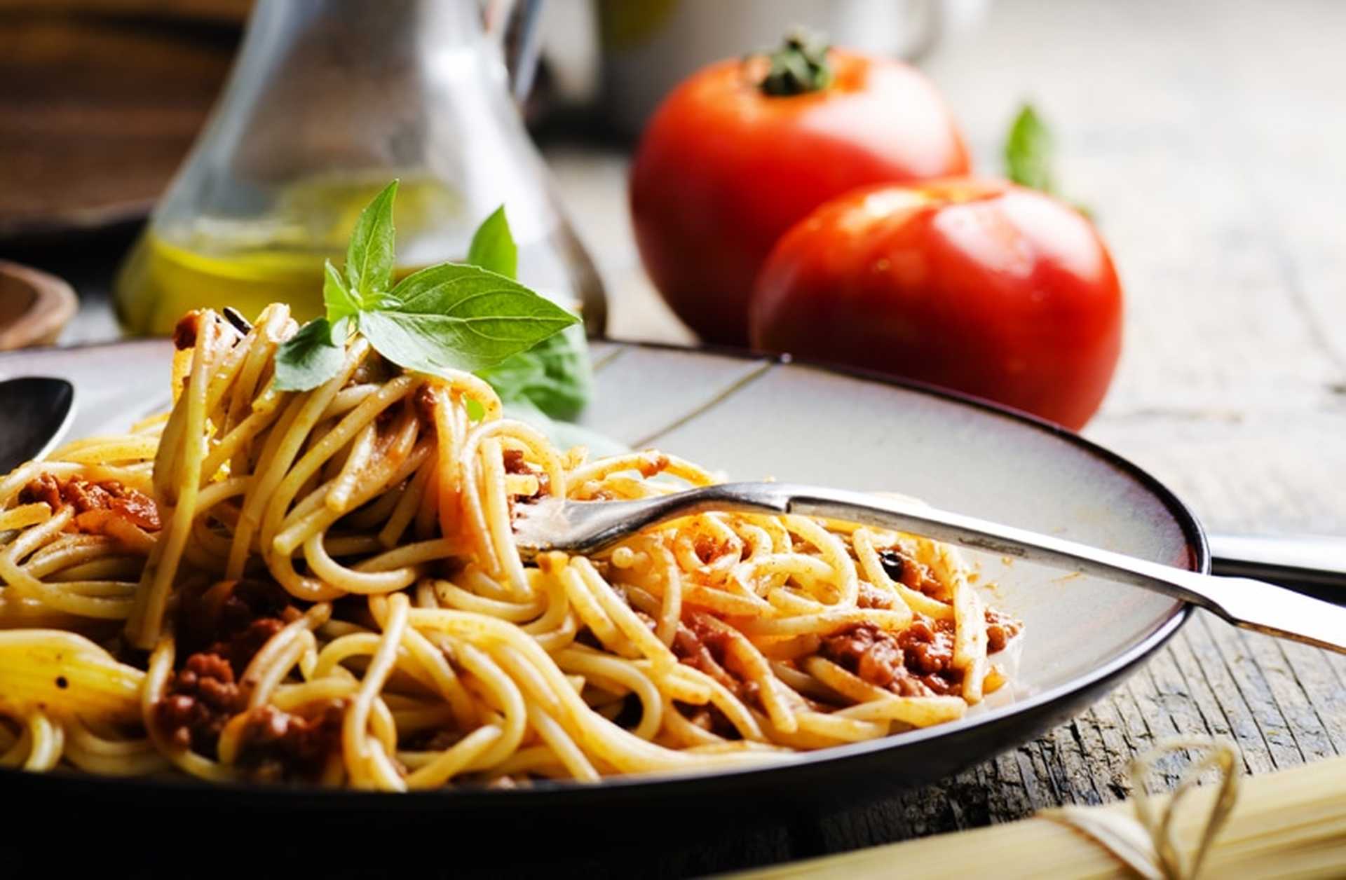A plate of spaghetti ragu with tomatoes and olive oil in the background
