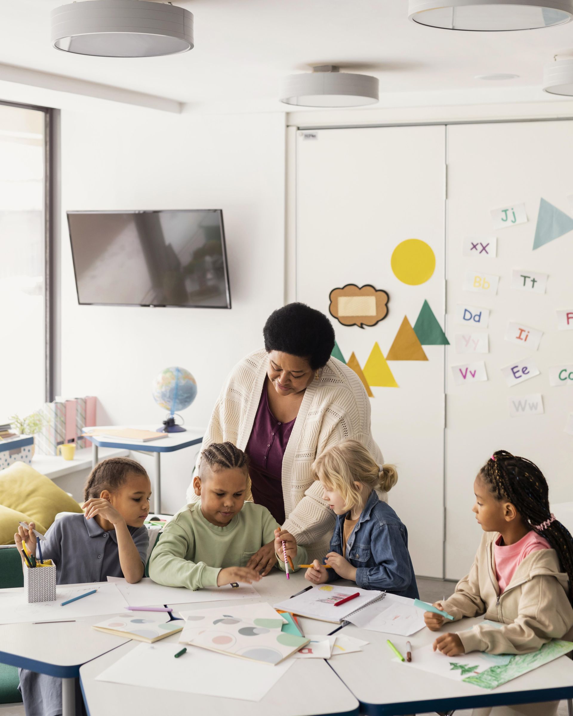 Children drawing in a classroom with a teacher helping